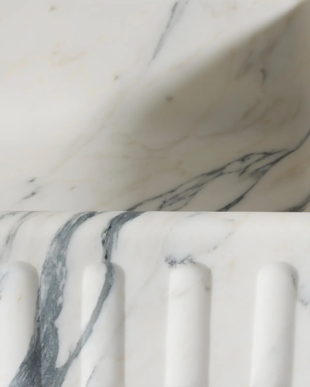 A close-up oblique view of the fluted front of an extra large single bowl Arabescato marble sink.
