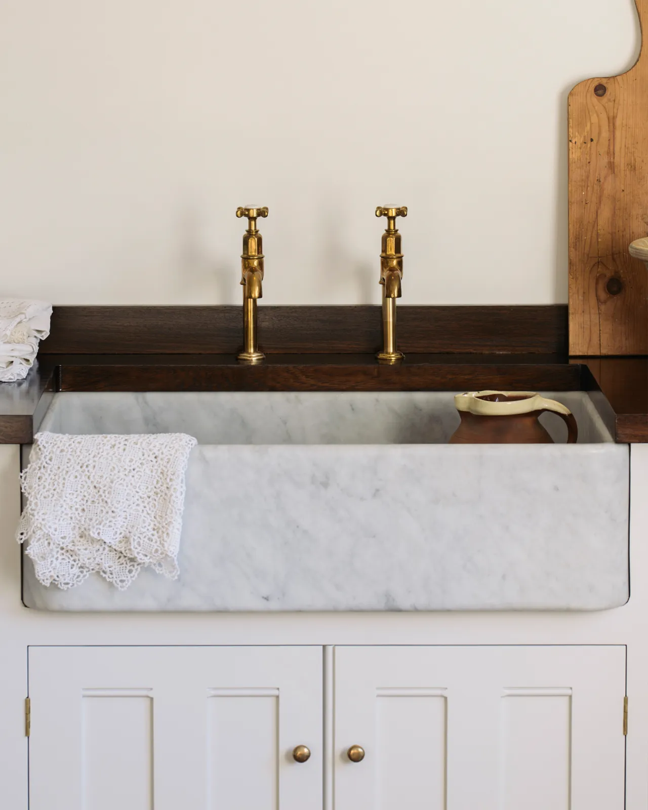 A close-up straight-on view of a large single bowl Carrara marble sink in a white painted Georgian-style kitchen sink cabinet with a dark hardwood worktop.