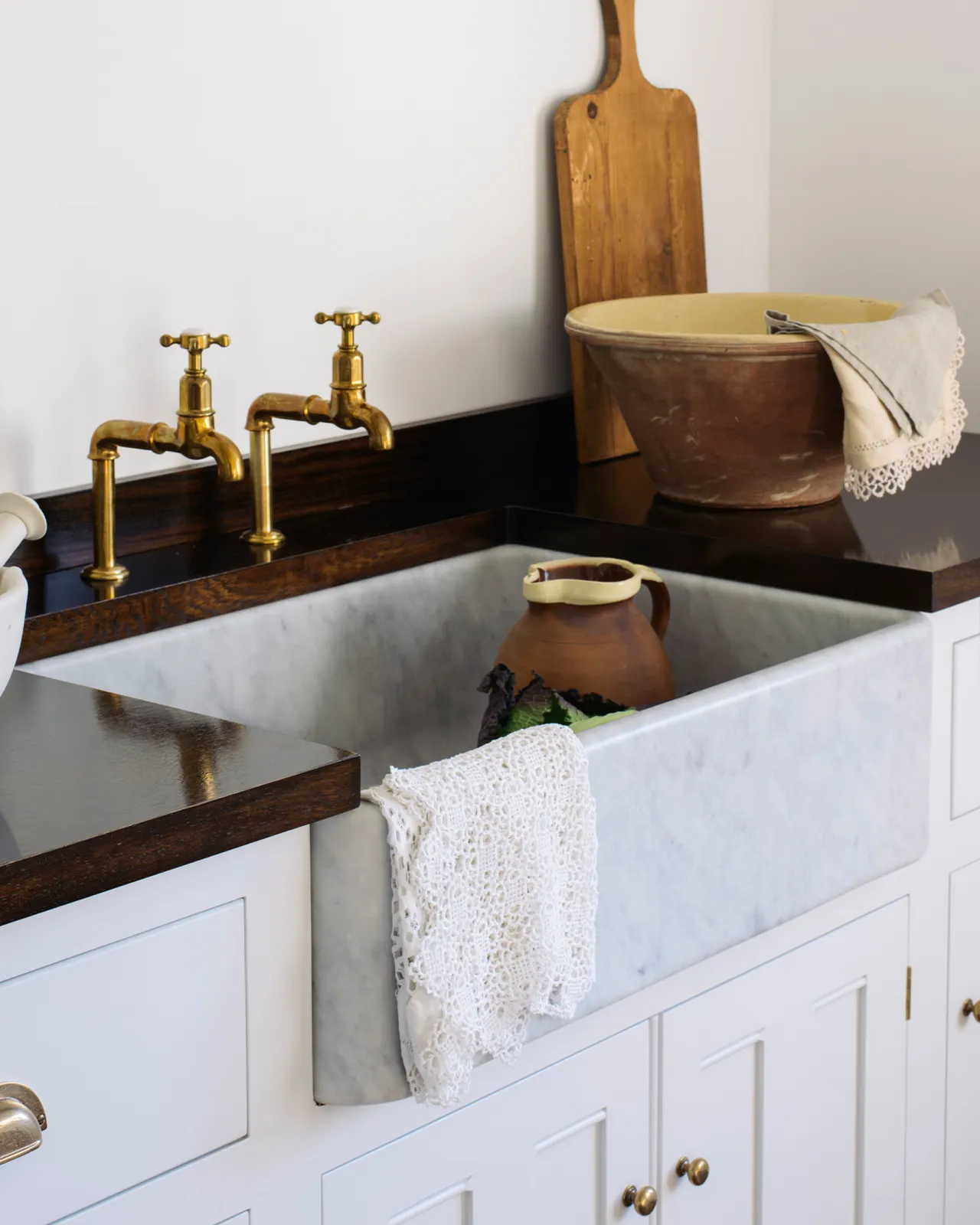 A close-up oblique view of a large single bowl Carrara marble sink in a white painted Georgian-style kitchen sink cabinet with a dark hardwood worktop.
