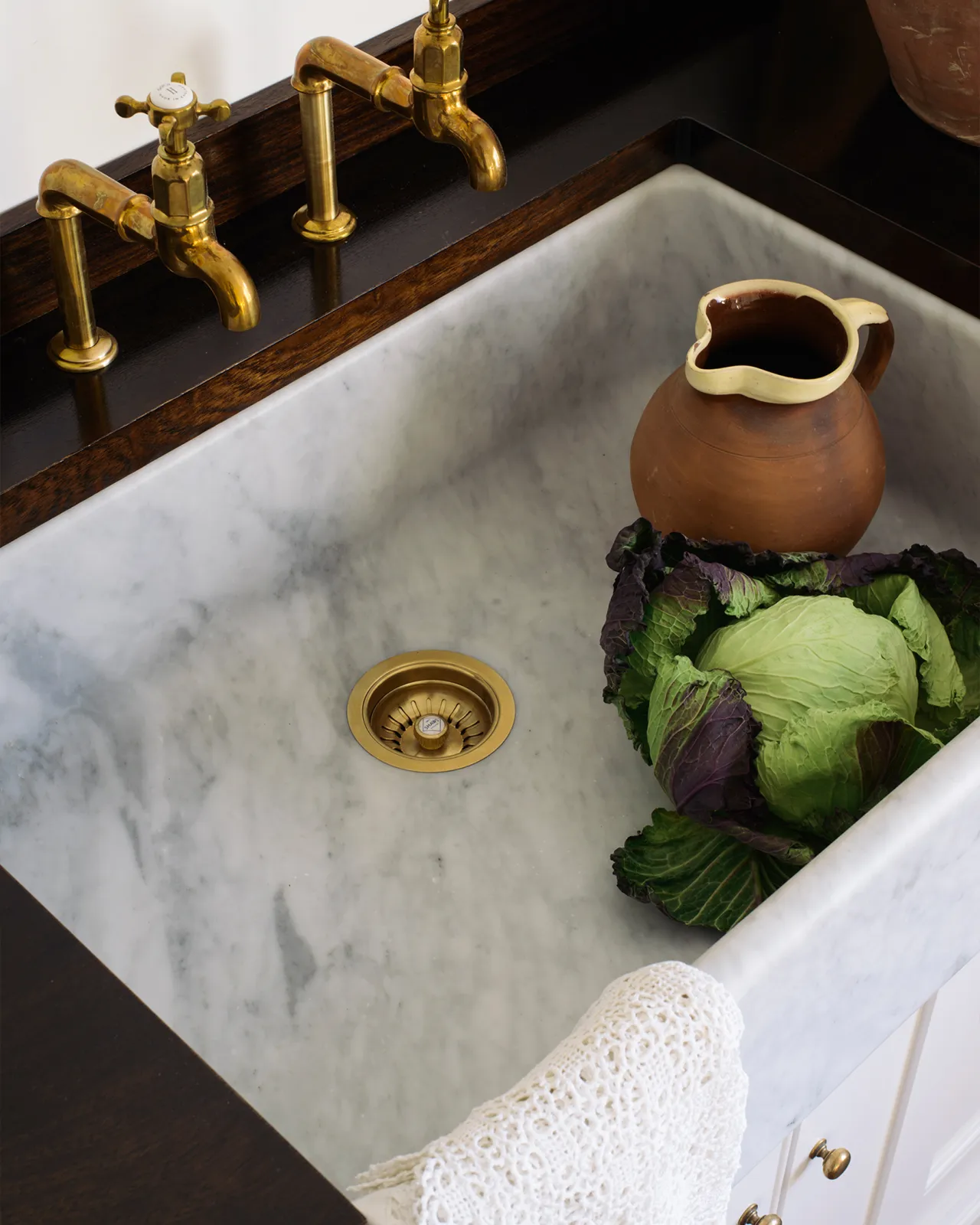 An overhead view of a large single bowl Carrara marble sink in a white painted Georgian-style kitchen sink cabinet with a dark hardwood worktop.
