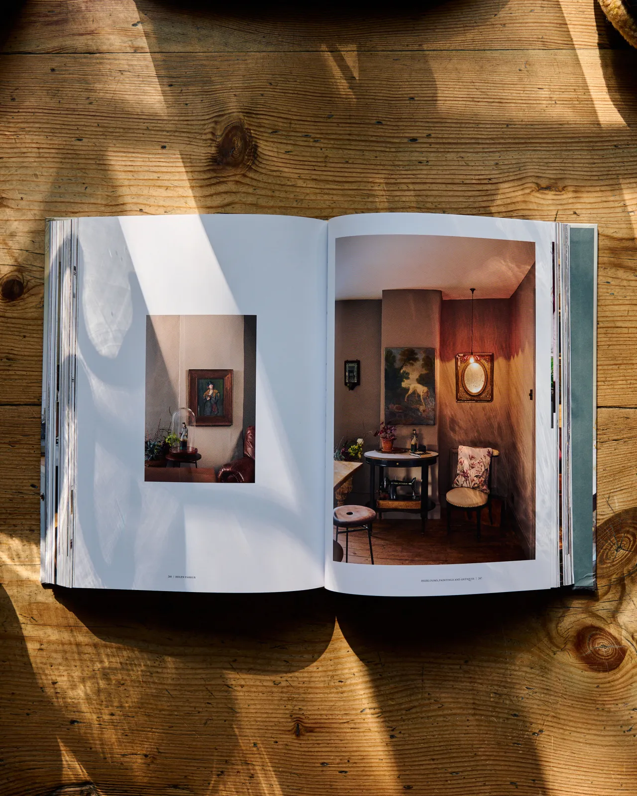A hardback book open to a page showing eclectic and traditional interior styling with vintage paintings, furniture and cranberry glass lighting.
