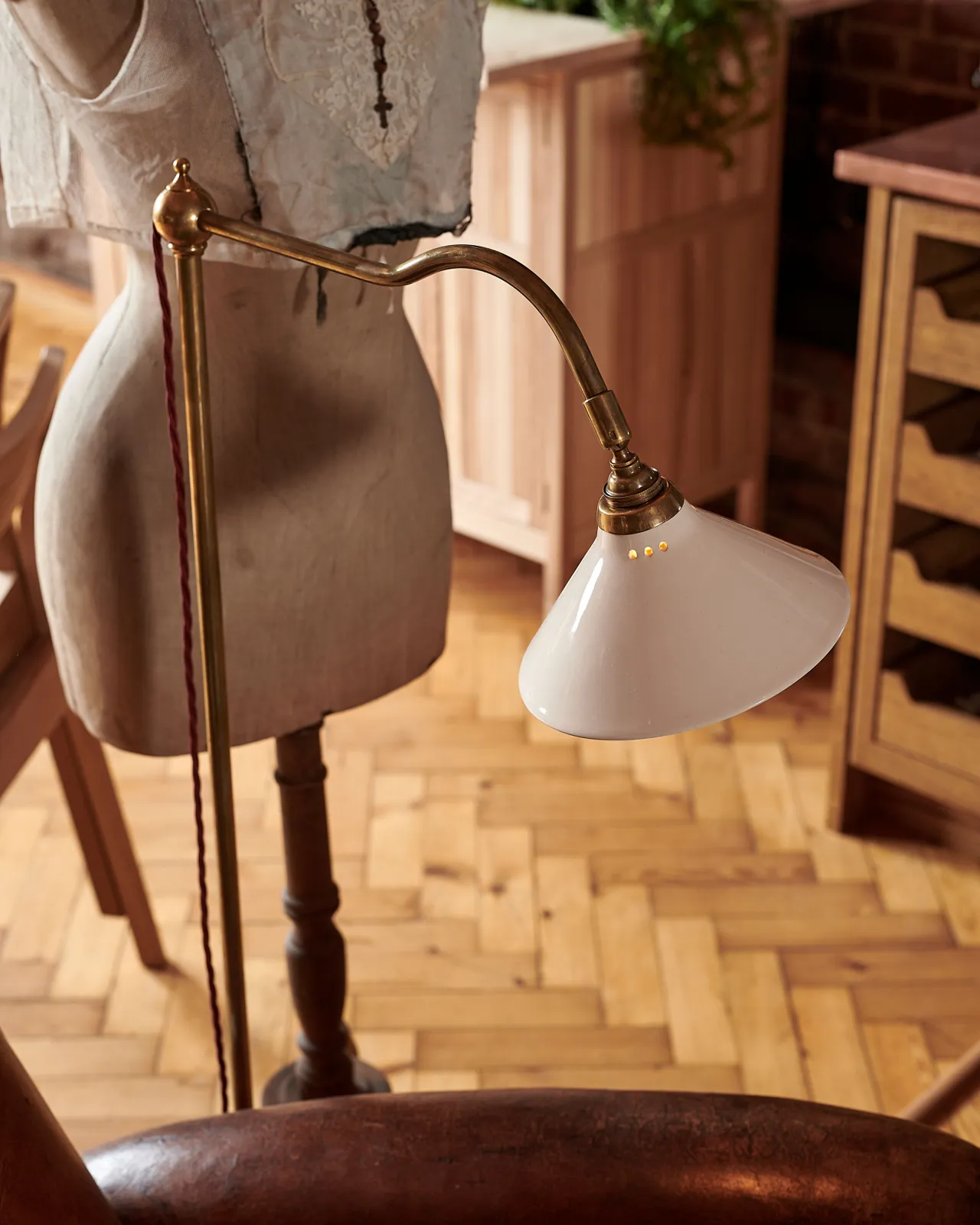 An oblique view of a small cream glazed ceramic light shade fitted to a curved brass arm with a pointed finial.