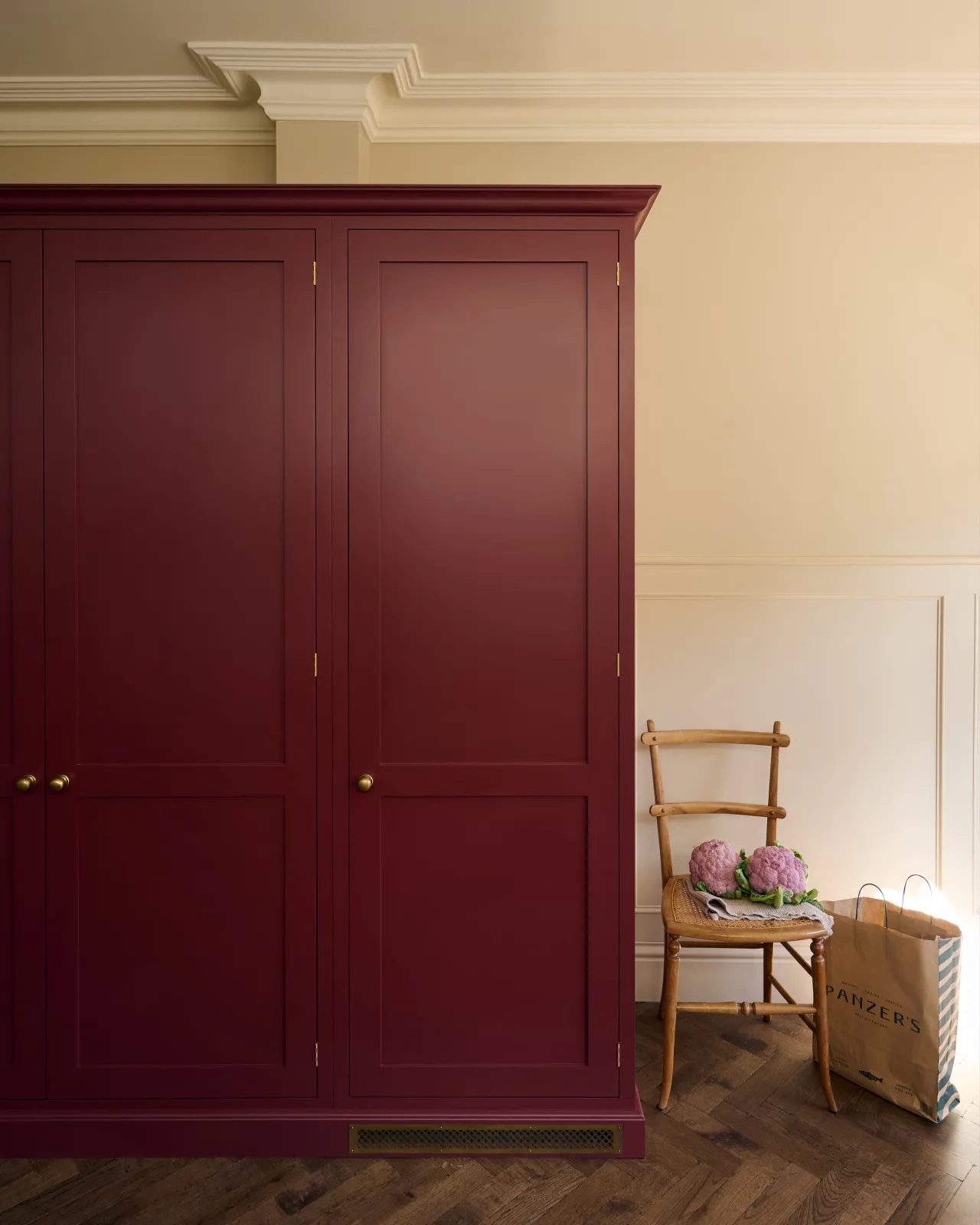 A straight-on view of a red painted Shaker-style pantry cupboard with a classic brass ventilation cover fitted to the skirting.