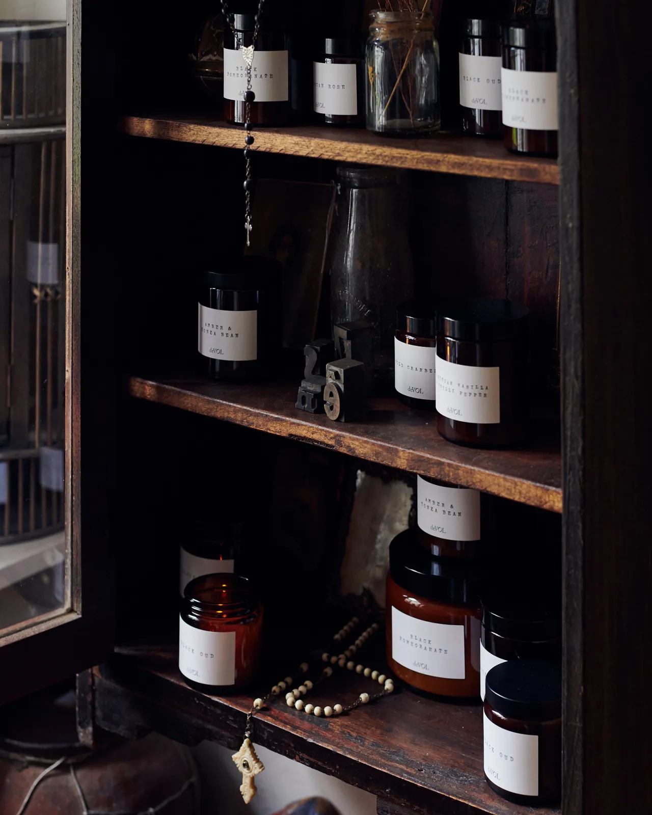 A collection of scented candles in brown glass jars with black lids in a vintage cupboard.