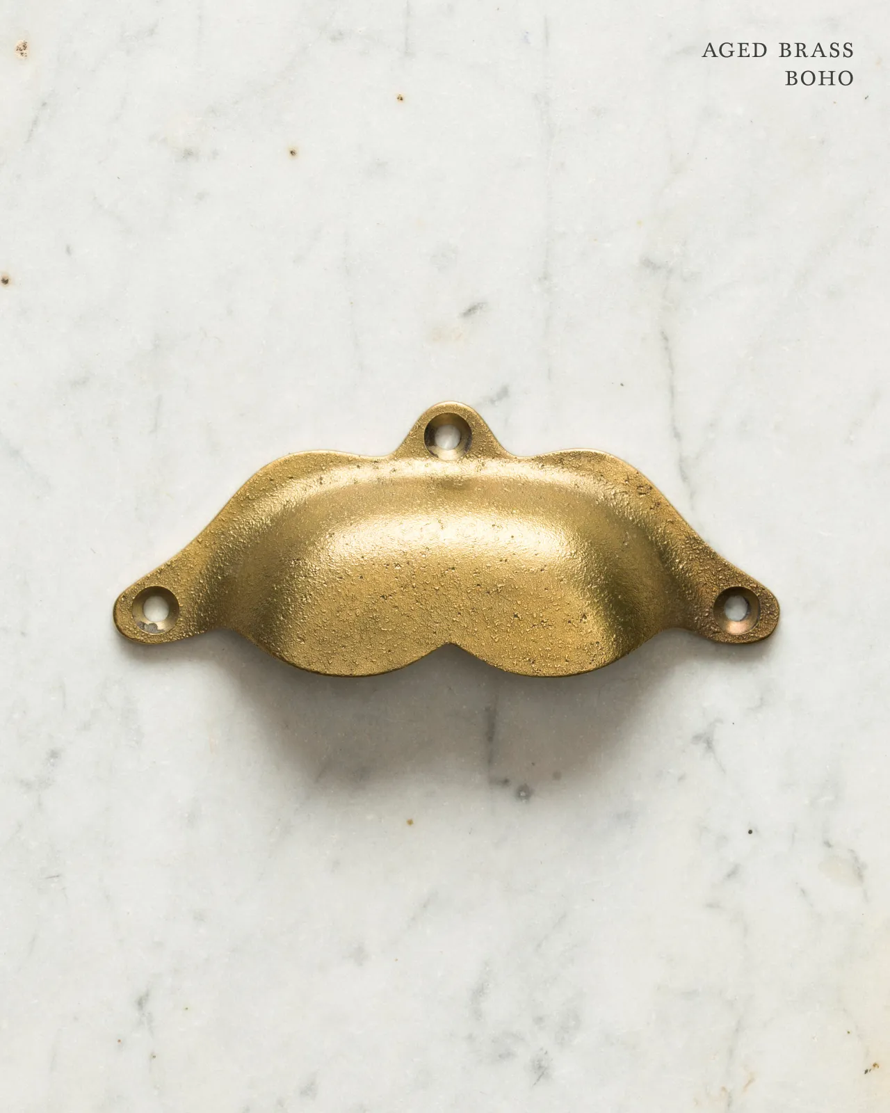A bohemian-style cup handle for a kitchen cupboard or drawer with an aged brass finish.