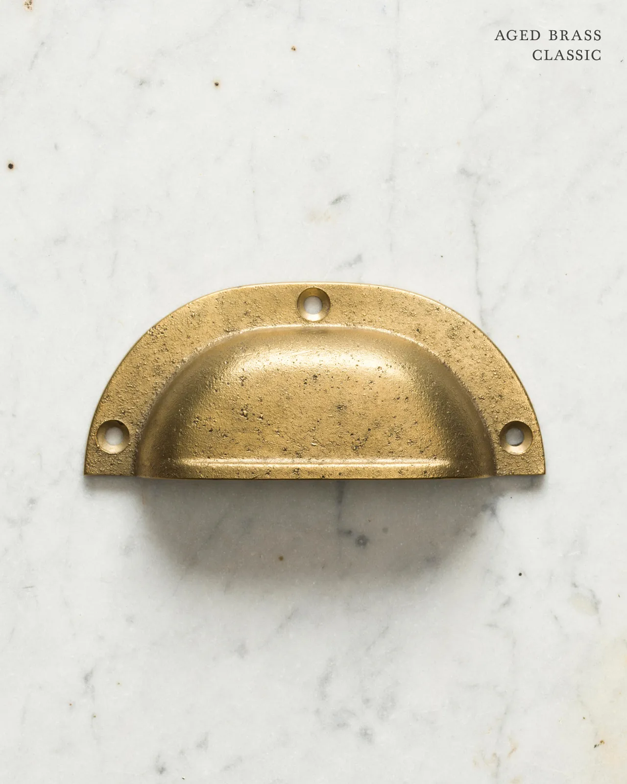 A classic cup handle for a kitchen cupboard or drawer with an aged brass finish.