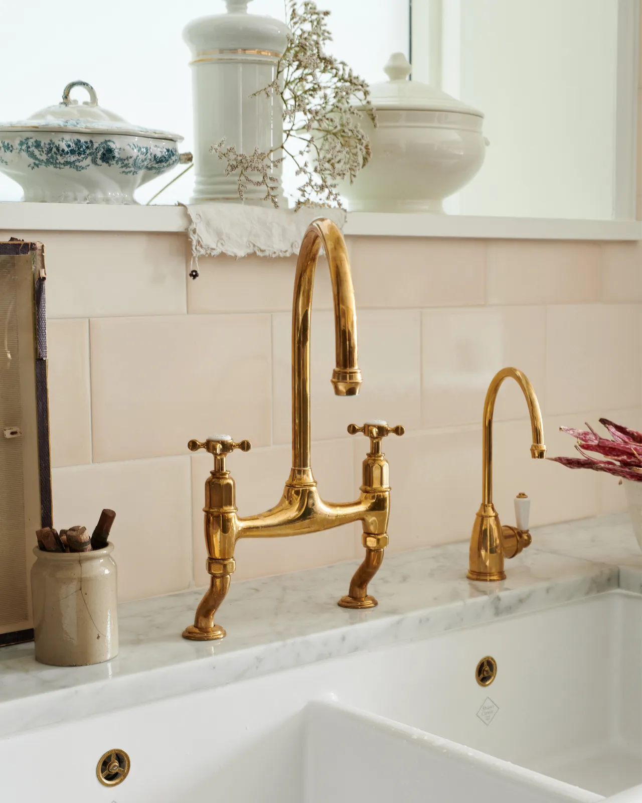 An oblique view of a traditional-style aged brass mixer tap with crosshead handles, beside a smaller brass tap.