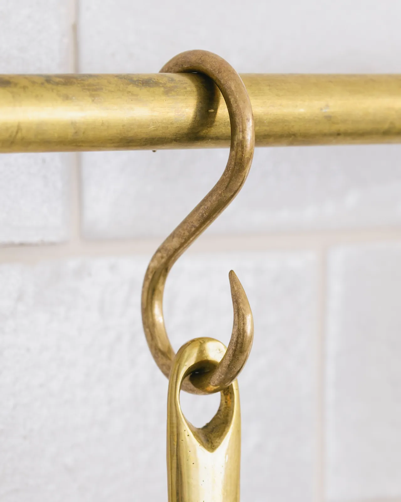 A close-up view of a brass s hook hanging from a brass rail.