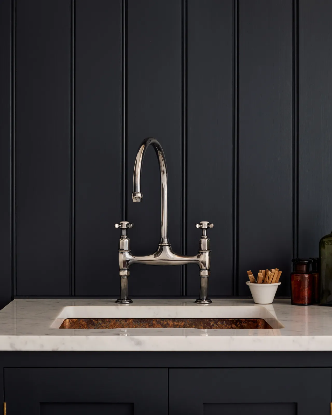 A straight-on view of a traditional-style tarnished silver mixer tap with crosshead handles in a classic utility kitchen with a Carrara marble worktop and deep blue painted cupboards and tongue and groove panelling.