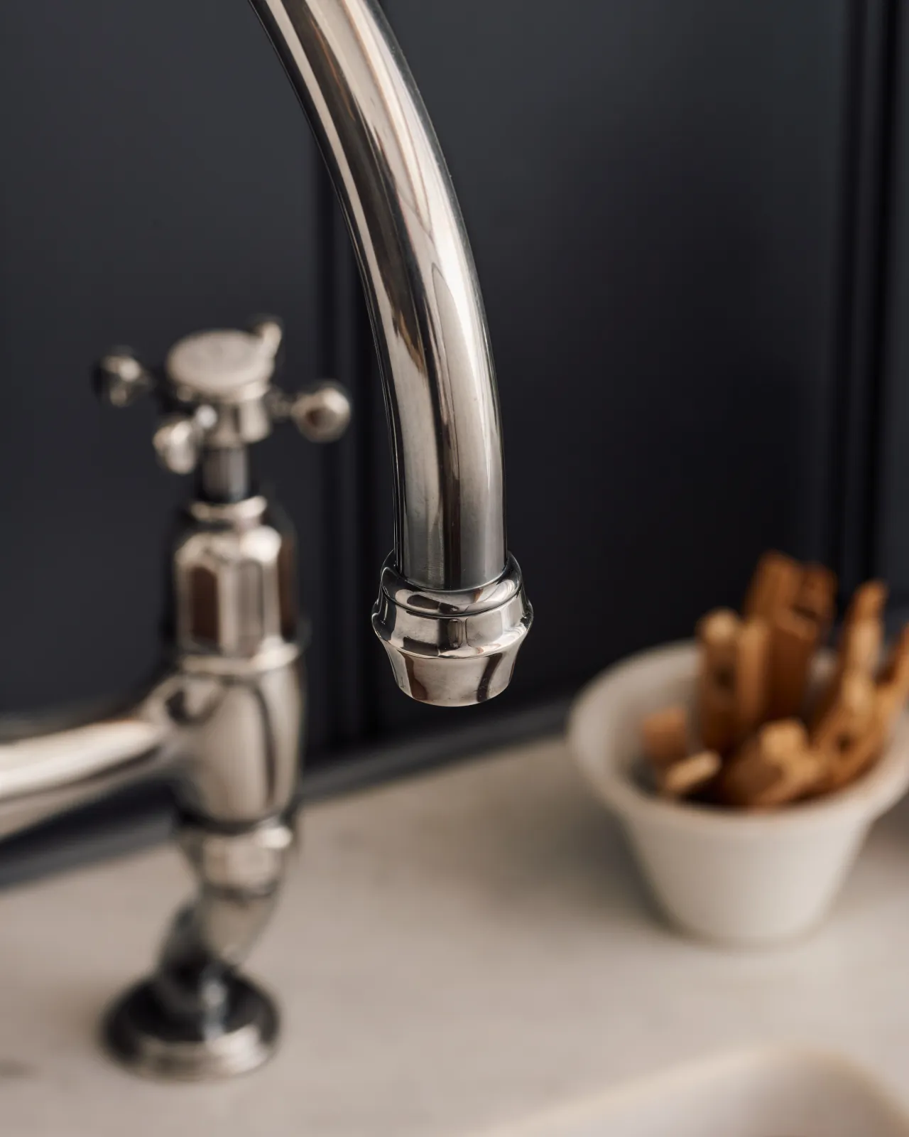 A close-up view of the spout of a traditional-style tarnished silver mixer tap with crosshead handles.