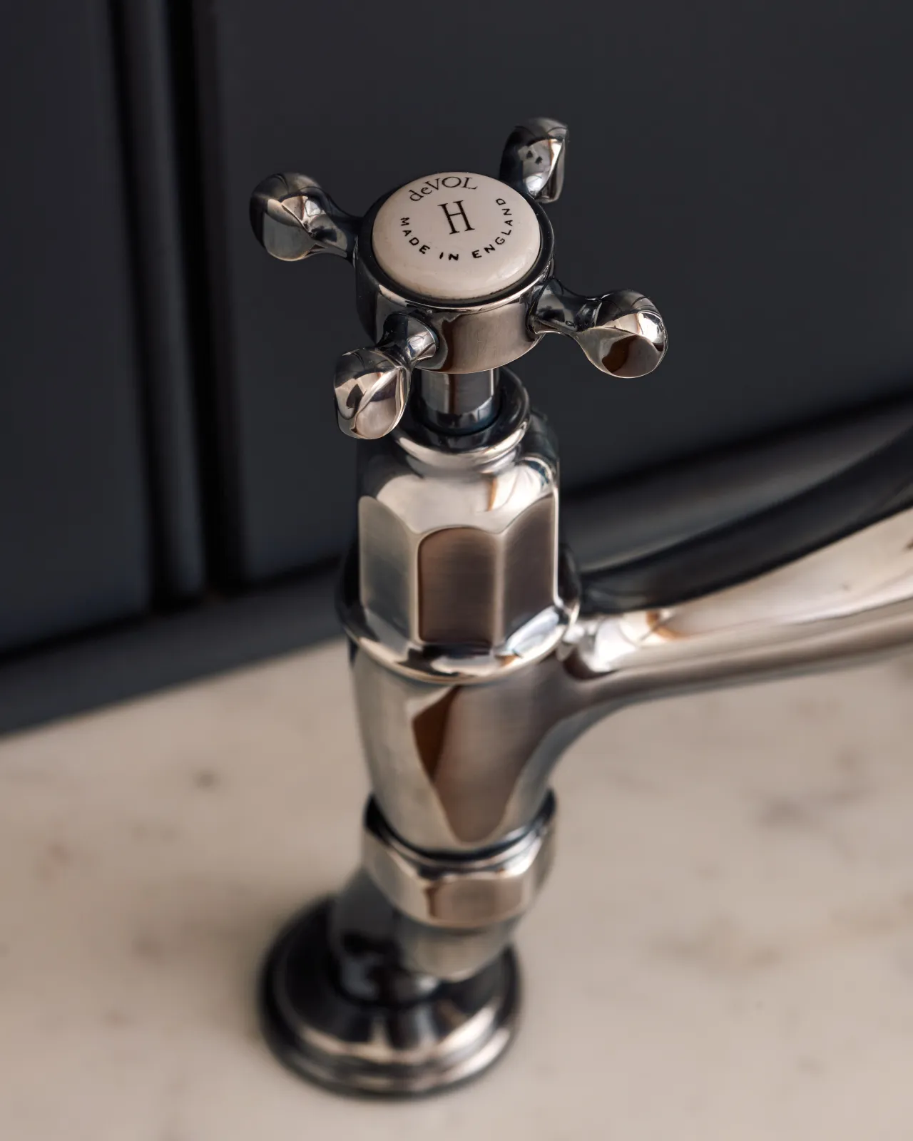A close-up view of a crosshead handle of a traditional-style tarnished silver mixer tap. An 'H' can be seen in the centre of the handle with the words 'deVOL' and 'Made in England' around the perimeter.