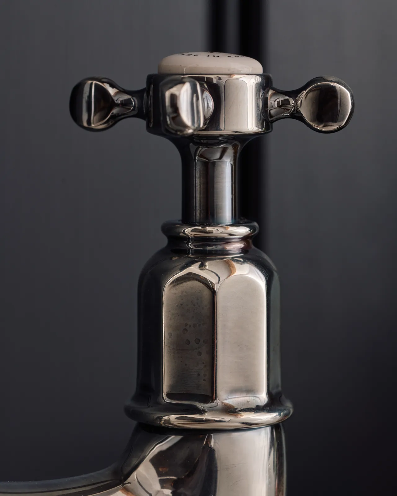 A close-up profile view of a crosshead handle of a traditional-style tarnished silver mixer tap.