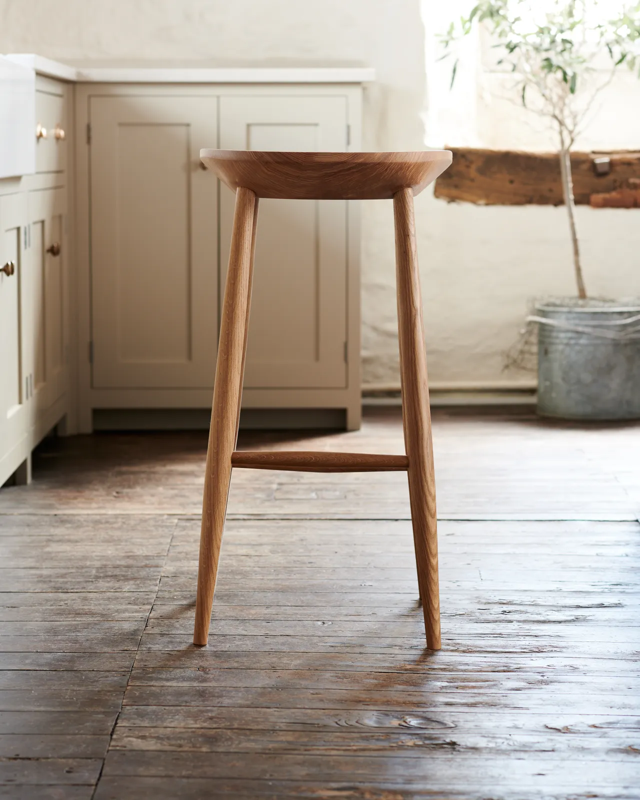 A straight-on view of the back of a mid-century-style bar stool with a sculpted ash seat pan and oak legs.