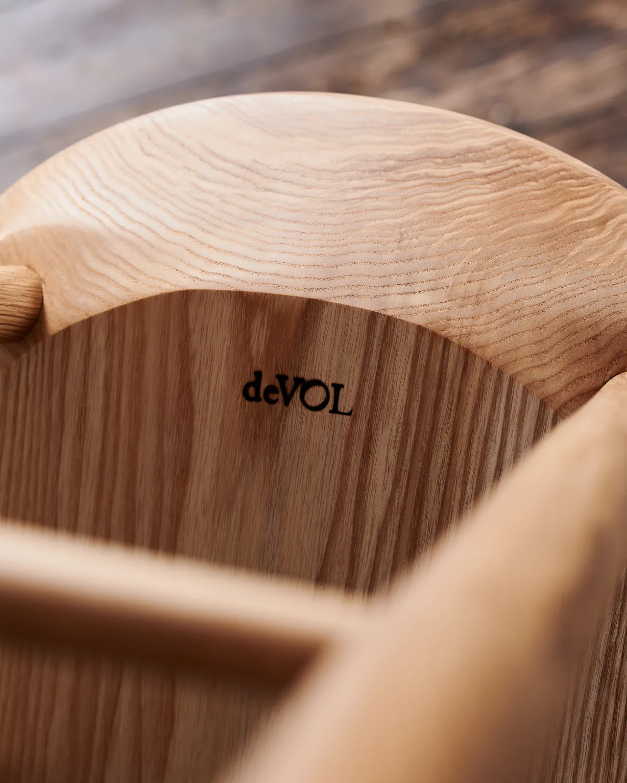 A close-up view of the underside of the ash seat pan from a mid-century-style bar stool, showing a small black 'deVOL' logo.