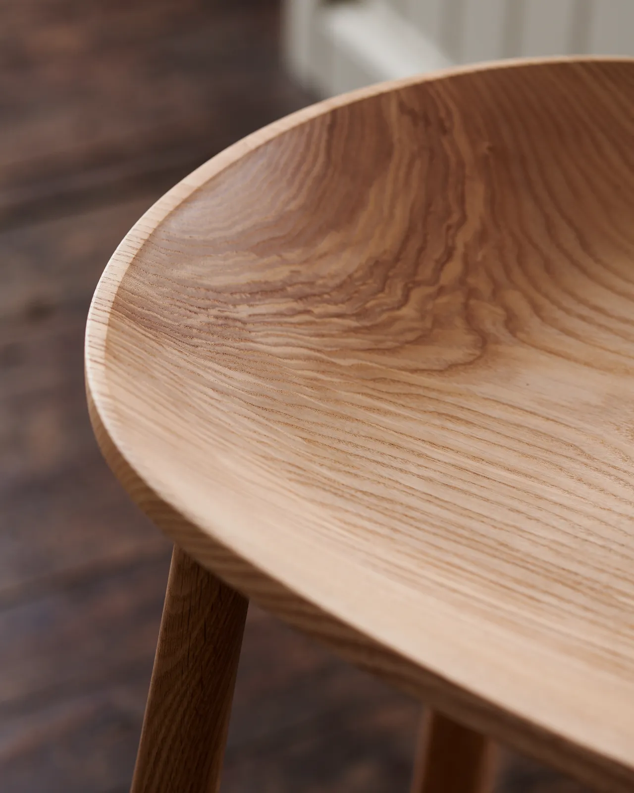 A close-up view of a sculpted ash seat pan from a mid-century-style bar stool.