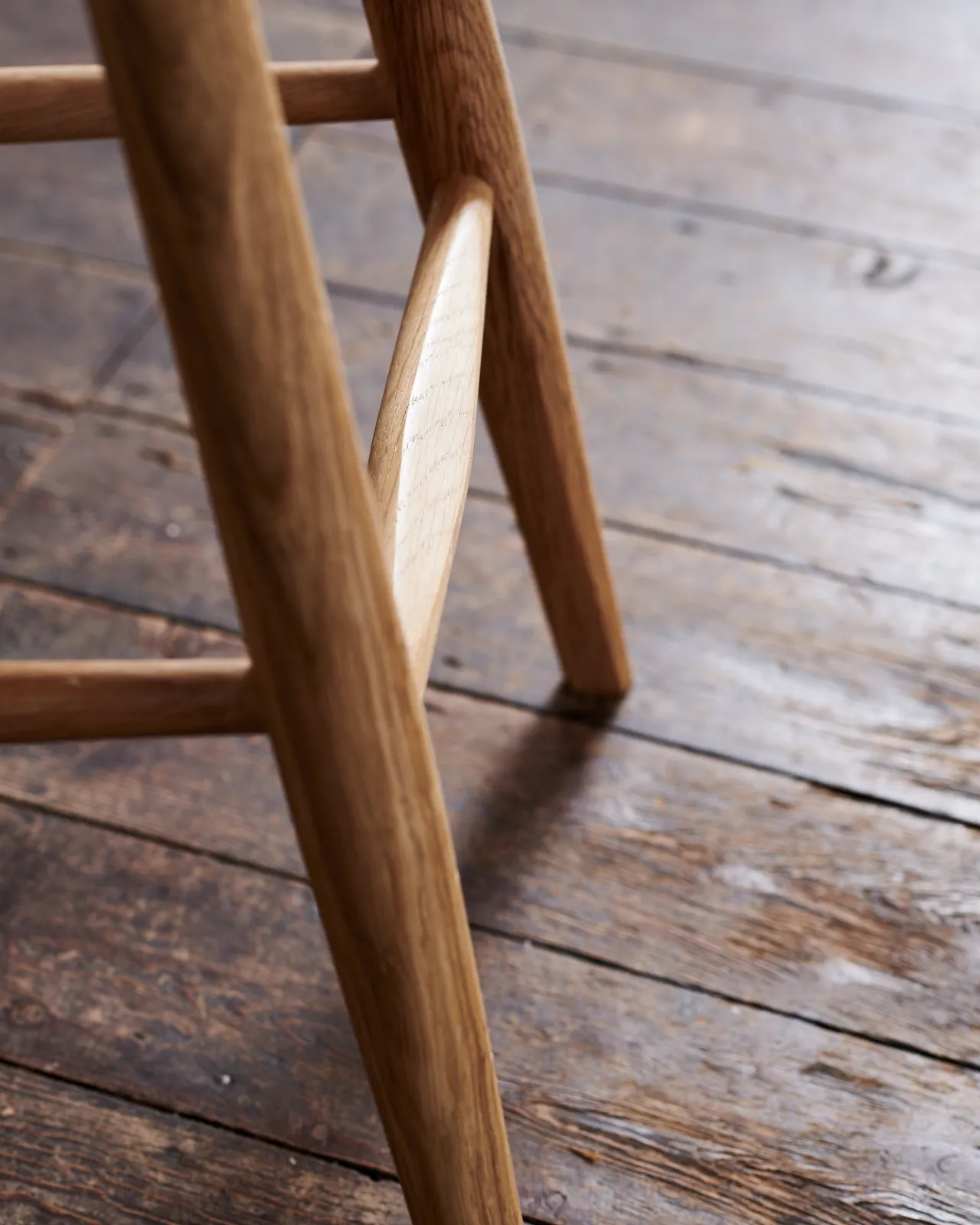 A close-up view of the oak footrest from a mid-century-style bar stool.