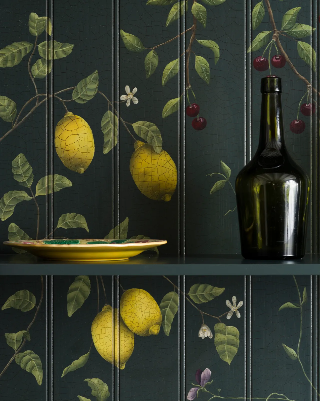 A close-up view of a dark green painted cupboard interior with hand-painted botanical flora, lemons and cherries on a tongue and groove-style backboard.