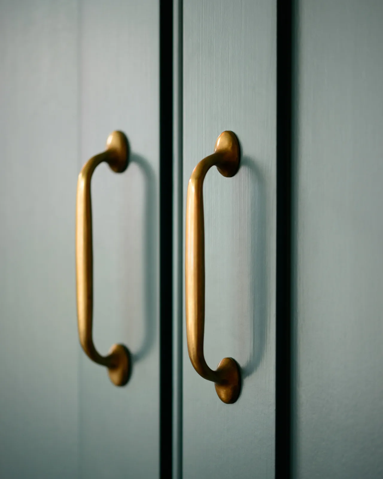 A pair of a simple pull handles in a burnished 'Bella' brass finish fitted to blue-green painted cupboard doors.