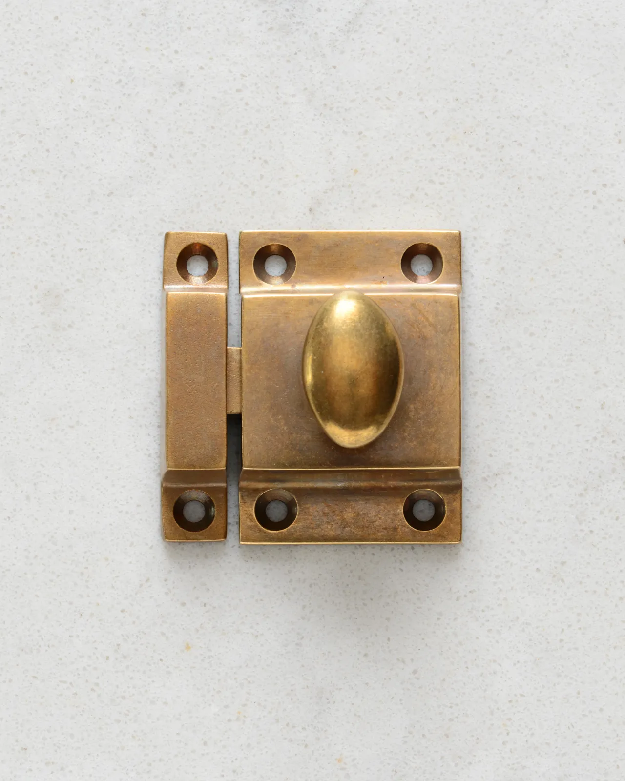 A square cupboard catch with an oval-shaped knob in a burnished 'Bella' brass finish.
