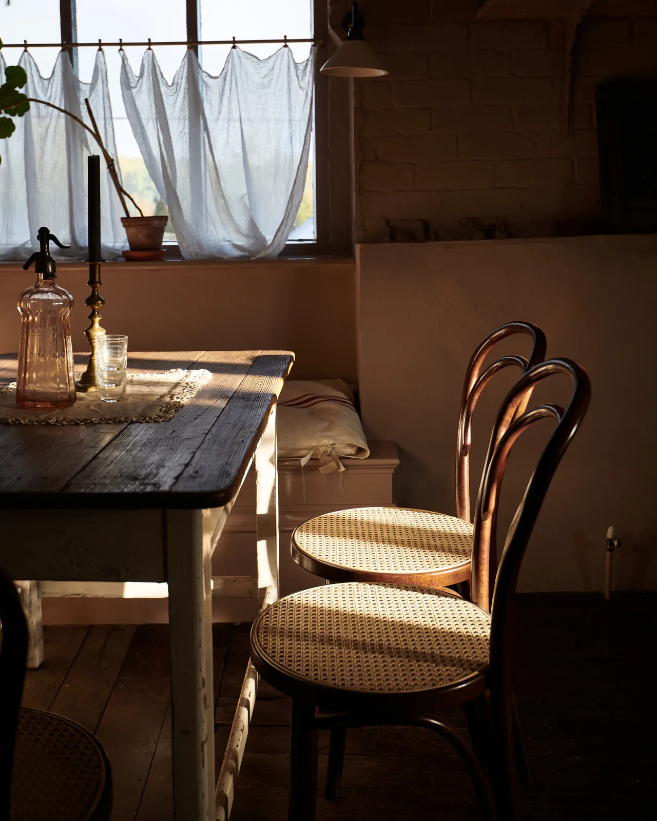 A vintage pine table with two café-style bentwood chairs with dark stained frames and light woven rattan seat mesh.