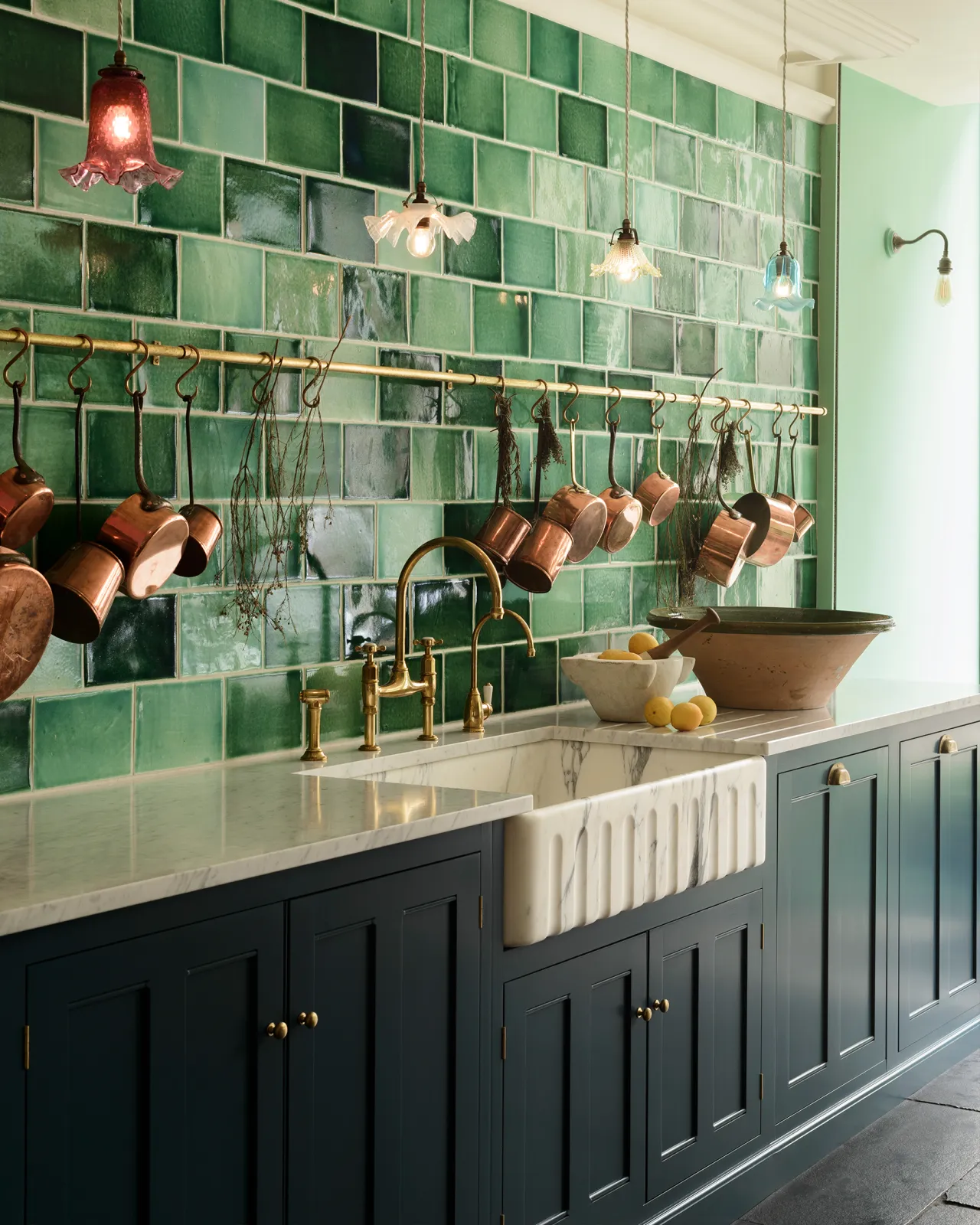 An oblique view of a grand Arabescato marble sink with a fluted front, with royal blue-coloured Georgian-style kitchen cupboards, aged brass taps and a wall of glossy emerald green tiles.