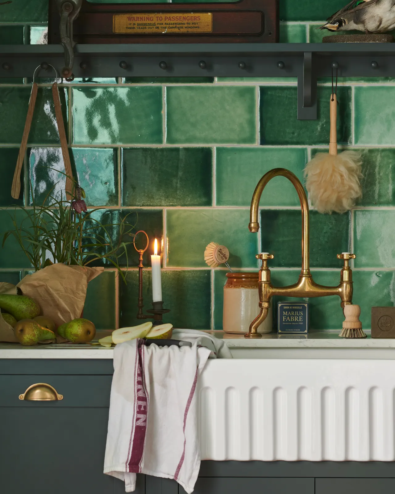 A straight-on view of a traditional-style aged brass mixer tap with crosshead handles. A wall of glossy emerald green tiles and eclectic styling surround the tap.