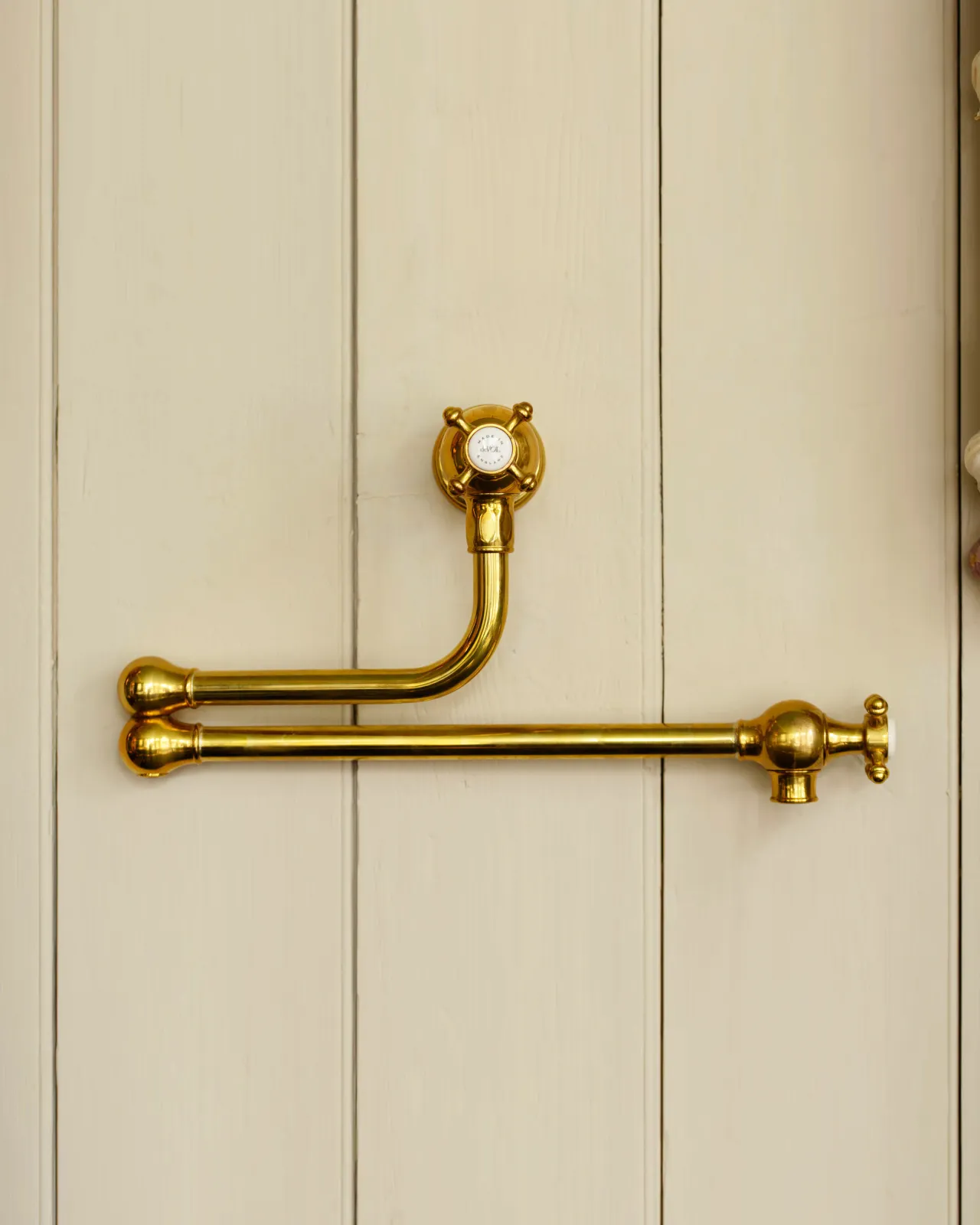 A traditional-style aged brass pot filler tap with crosshead handles fitted to a creamy coloured tongue and groove panelled wall.
