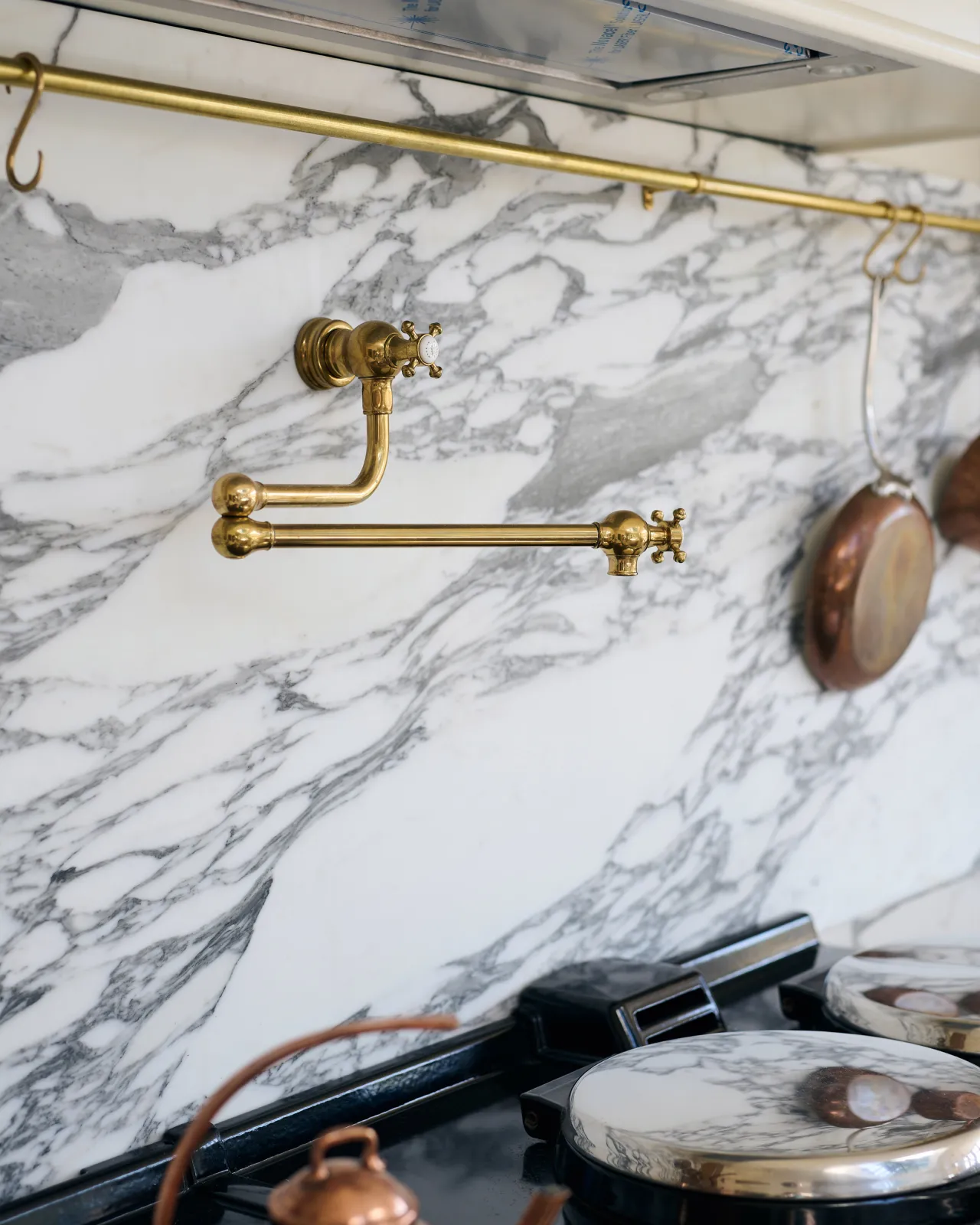 An oblique view of a traditional-style aged brass pot filler tap with crosshead handles fitted to an Arabescato marble splashback.