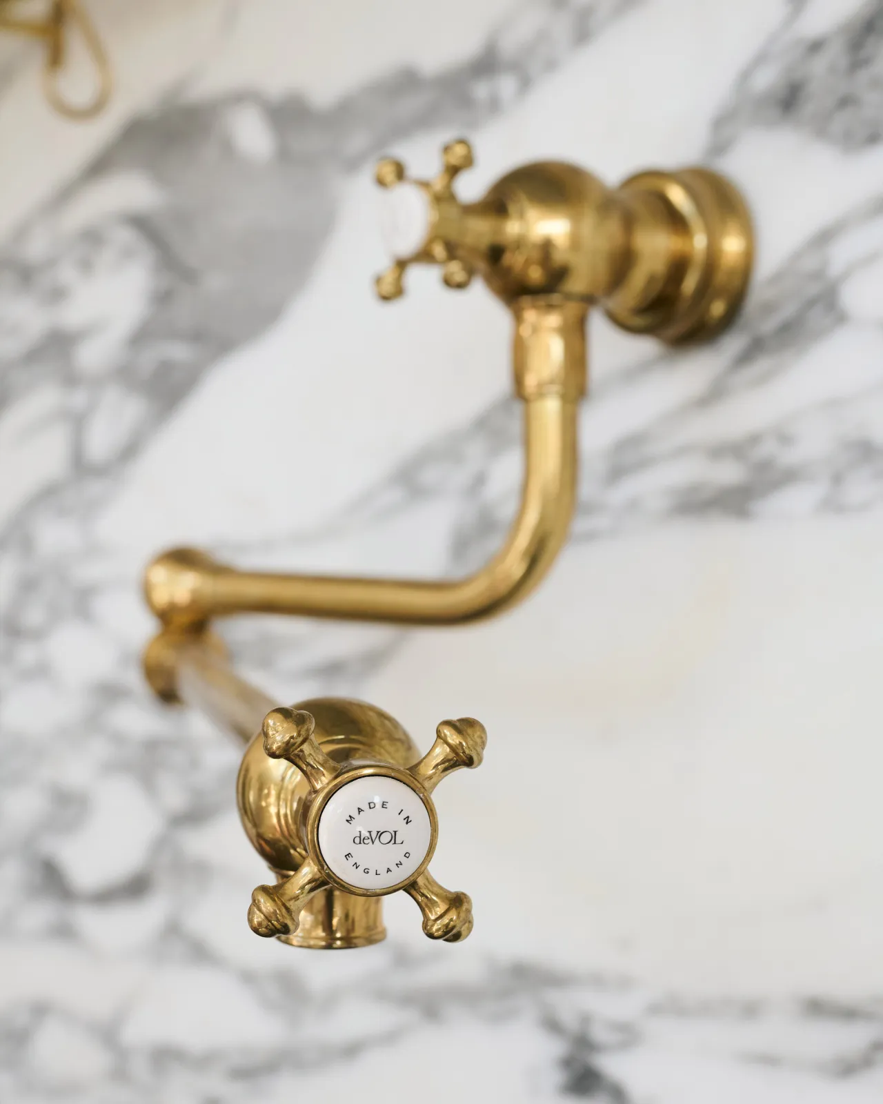 A close-up view of the crosshead handle at the spout of a traditional-style aged brass pot filler tap, a 'deVOL' logo can be seen in the centre of the handle.