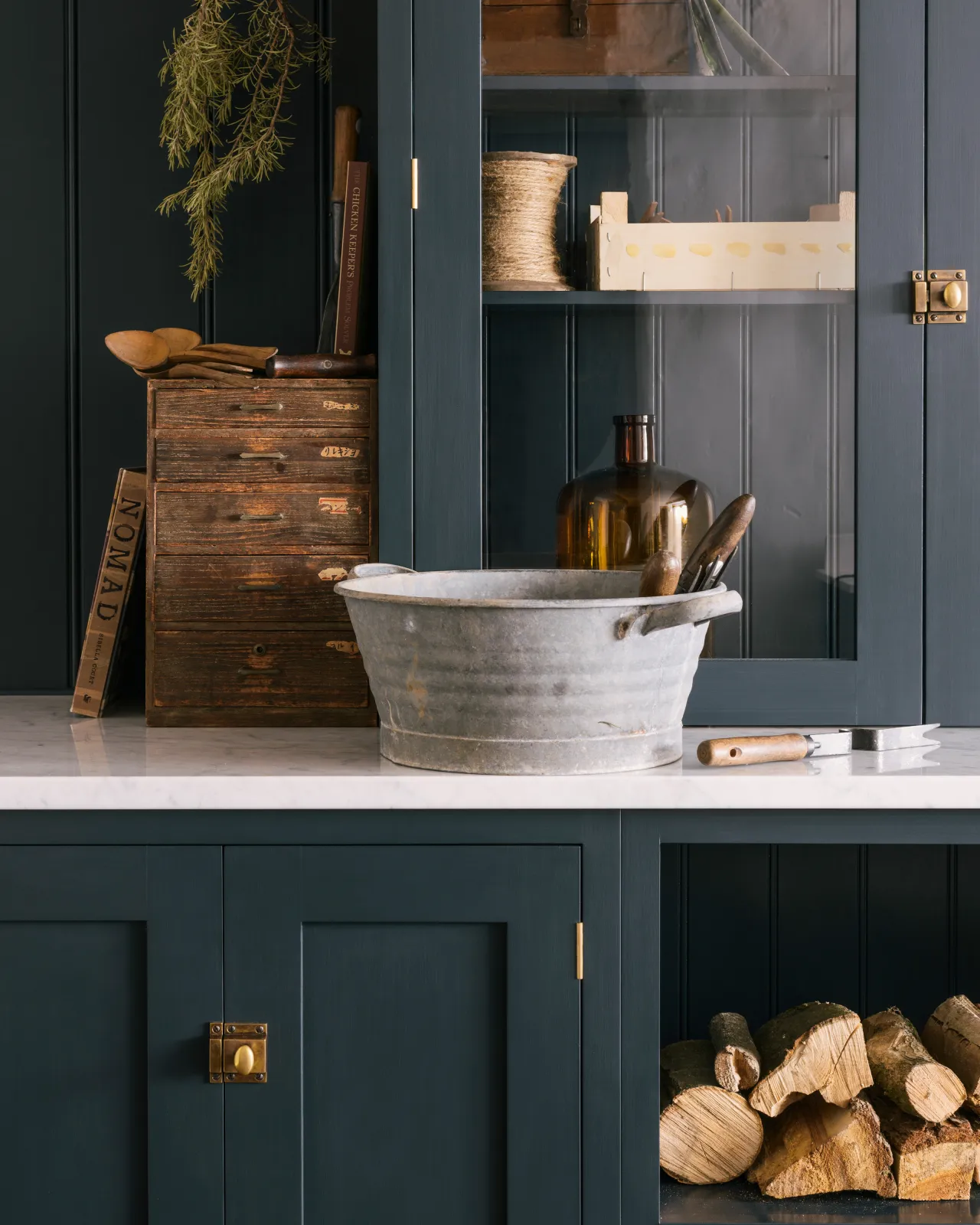 A close-up straight-on view of square cupboard catches in a burnished 'Bella' brass finish fitted to dark blue painted Shaker-style kitchen cupboards.