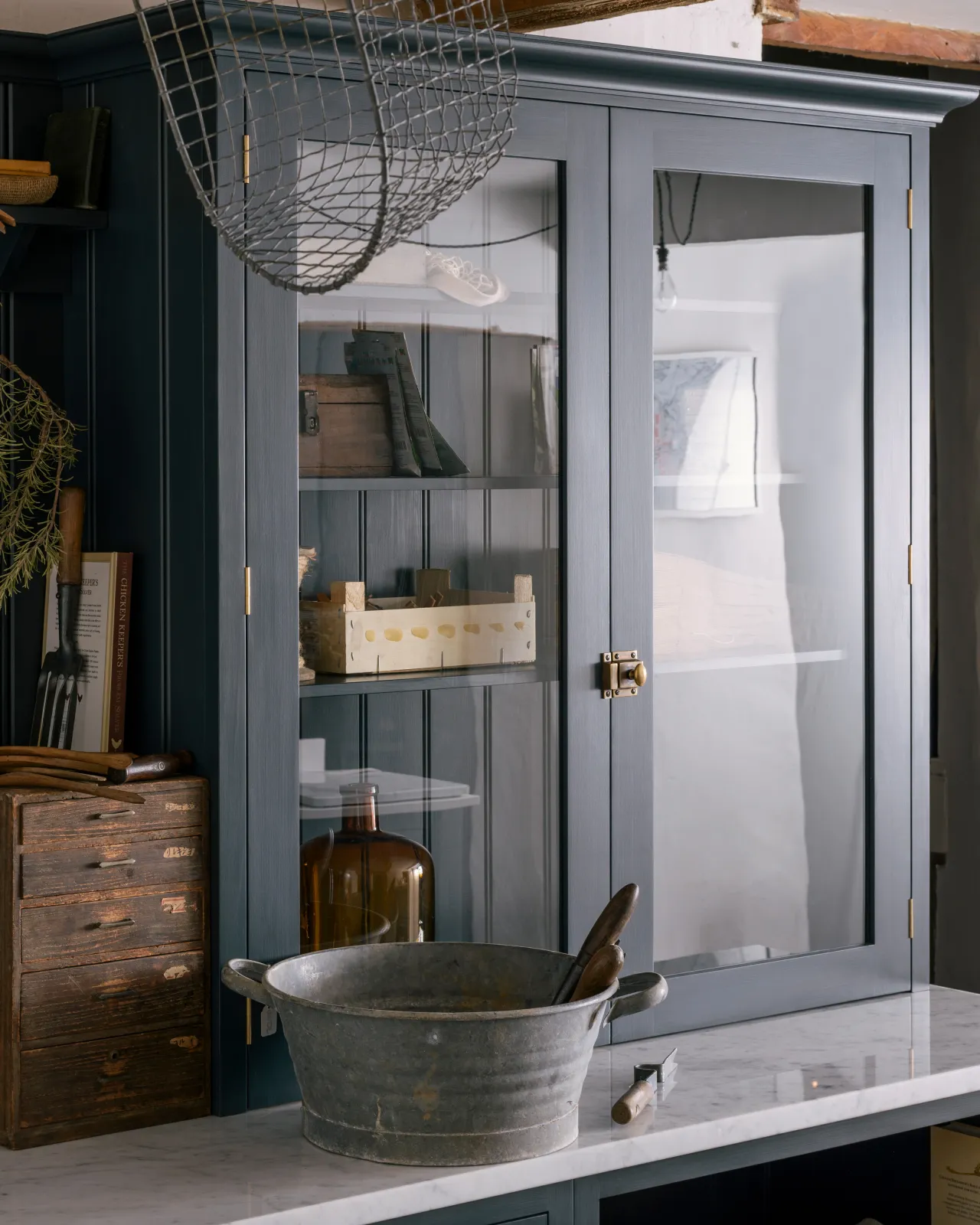 An oblique view of a Shaker-style countertop cupboard with glazed doors, dark blue painted frames and a square cupboard catch in a burnished 'Bella' brass finish.
