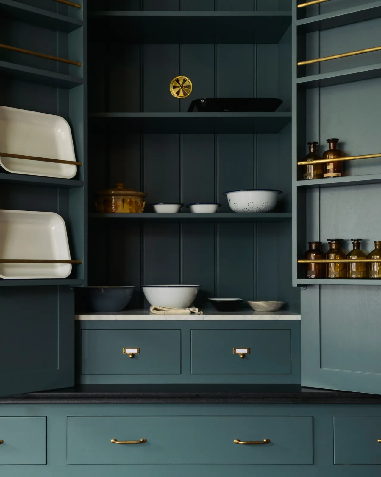Looking into an open Georgian-style countertop cupboard painted in a green-blue colour. There are two shallow drawers inside with burnished 'Bella' brass cardframe pull handles.