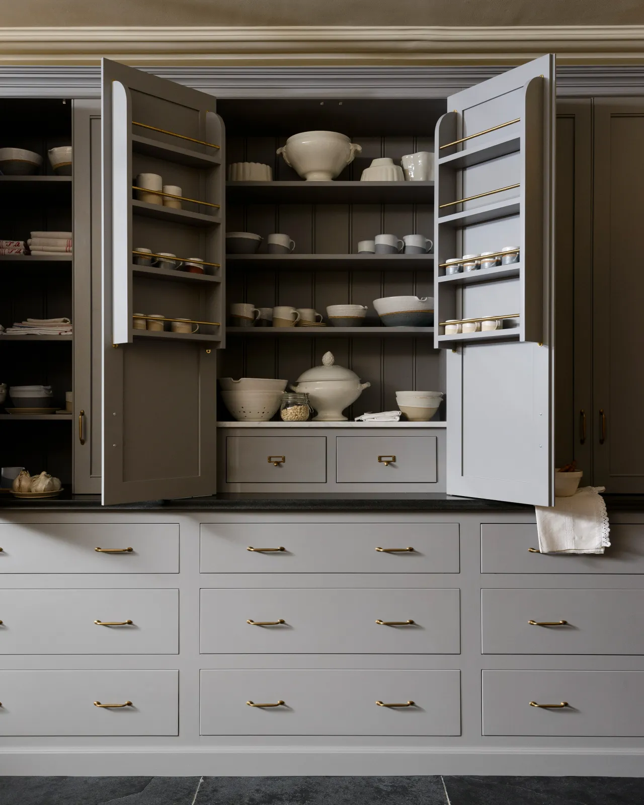 A Georgian-style larder cupboard painted in a grey colour. The countertop cupboard doors are open, revealing two shallow drawers inside with burnished 'Bella' brass cardframe pull handles.