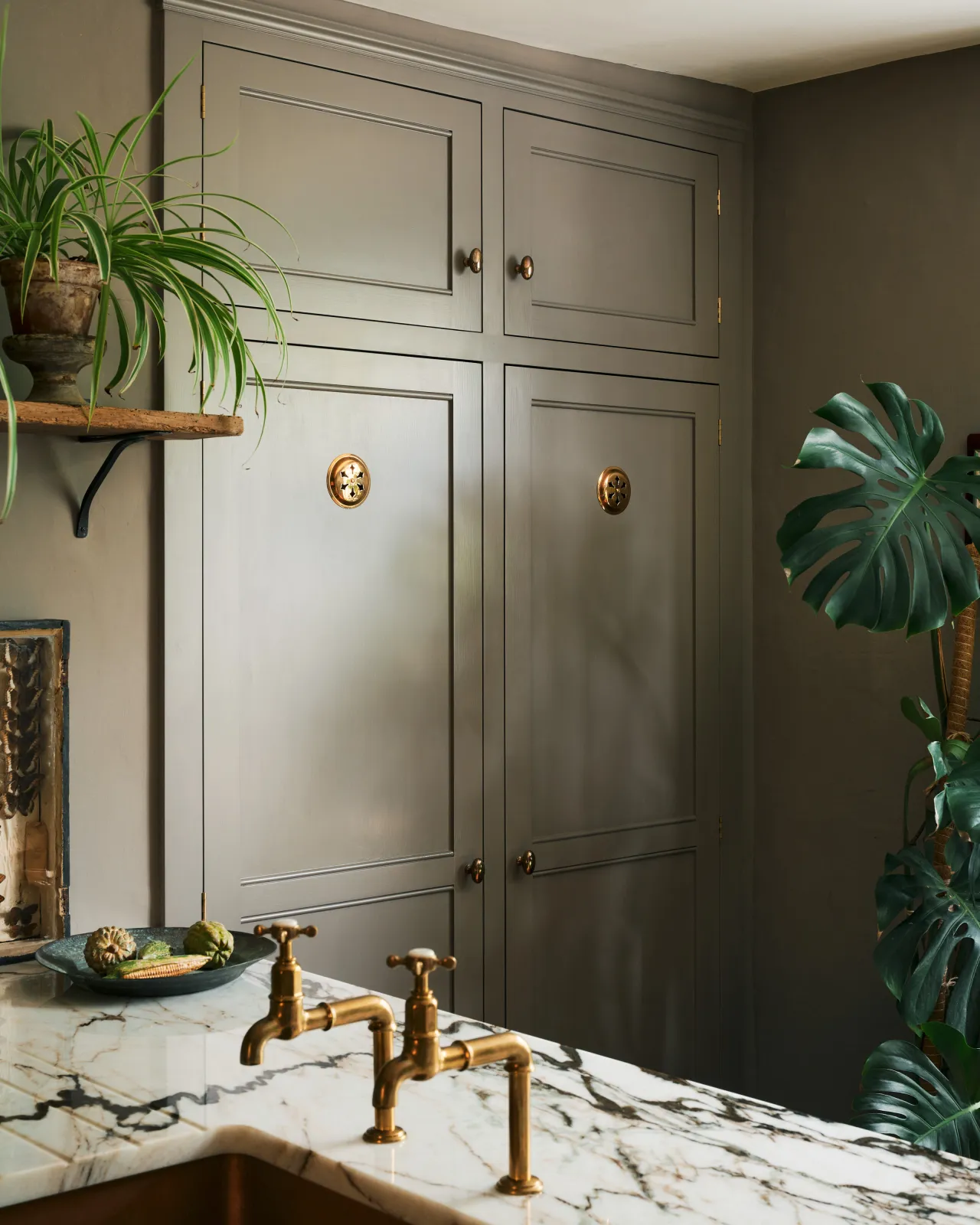 An oblique view of a grey painted fitted pantry with a pair of Victorian-inspired circular brass ventilation grilles with traditional decorative cutouts.
