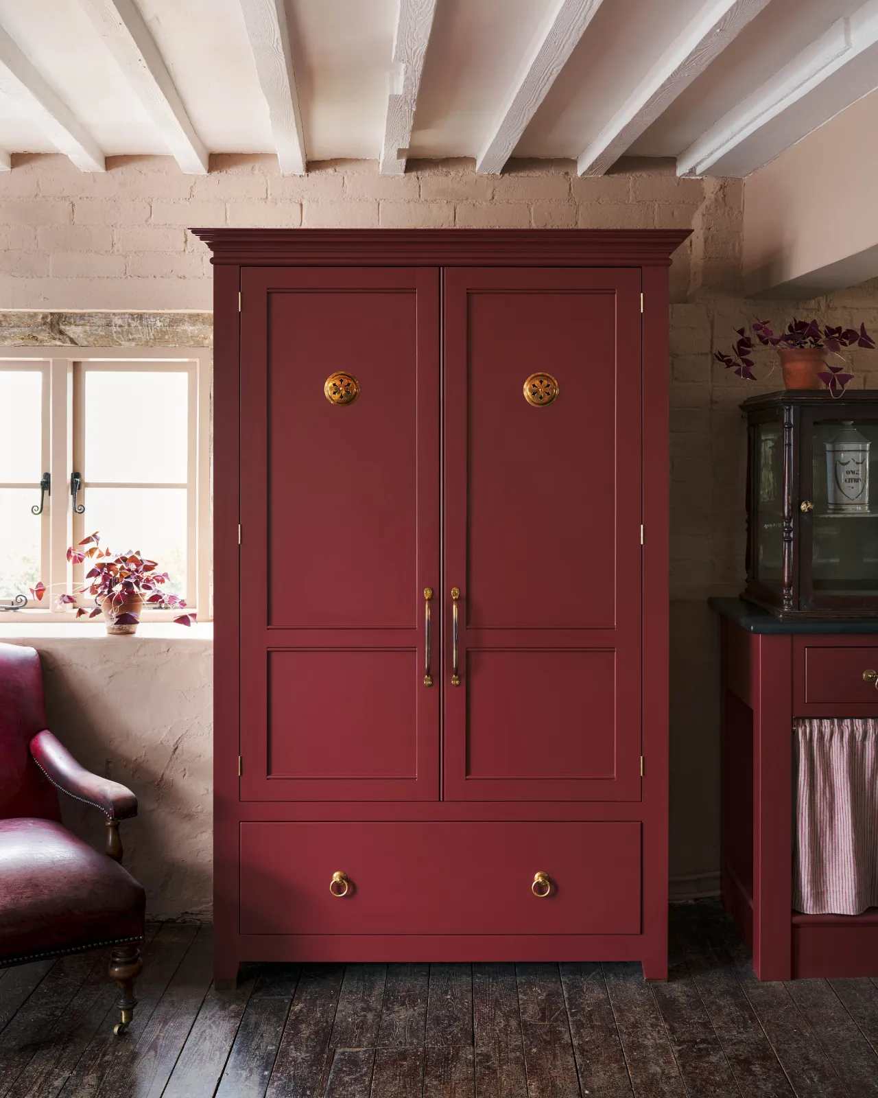 A red painted Georgian-style pantry cupboard with brass hardware and Victorian-inspired circular brass ventilation grilles fitted to each door.