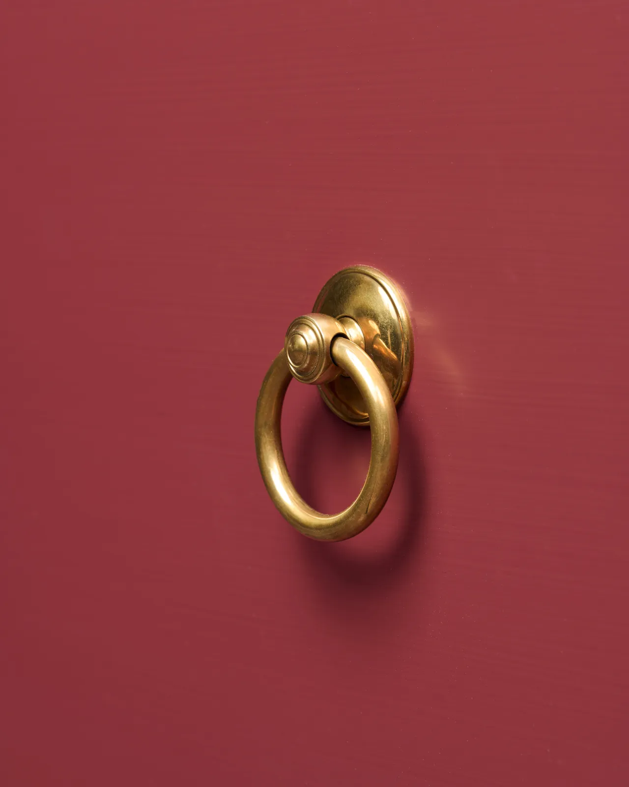 An oblique view of a Victorian-inspired ring pull handle in a warm burnished brass finish, fitted to a red painted cupboard drawer.