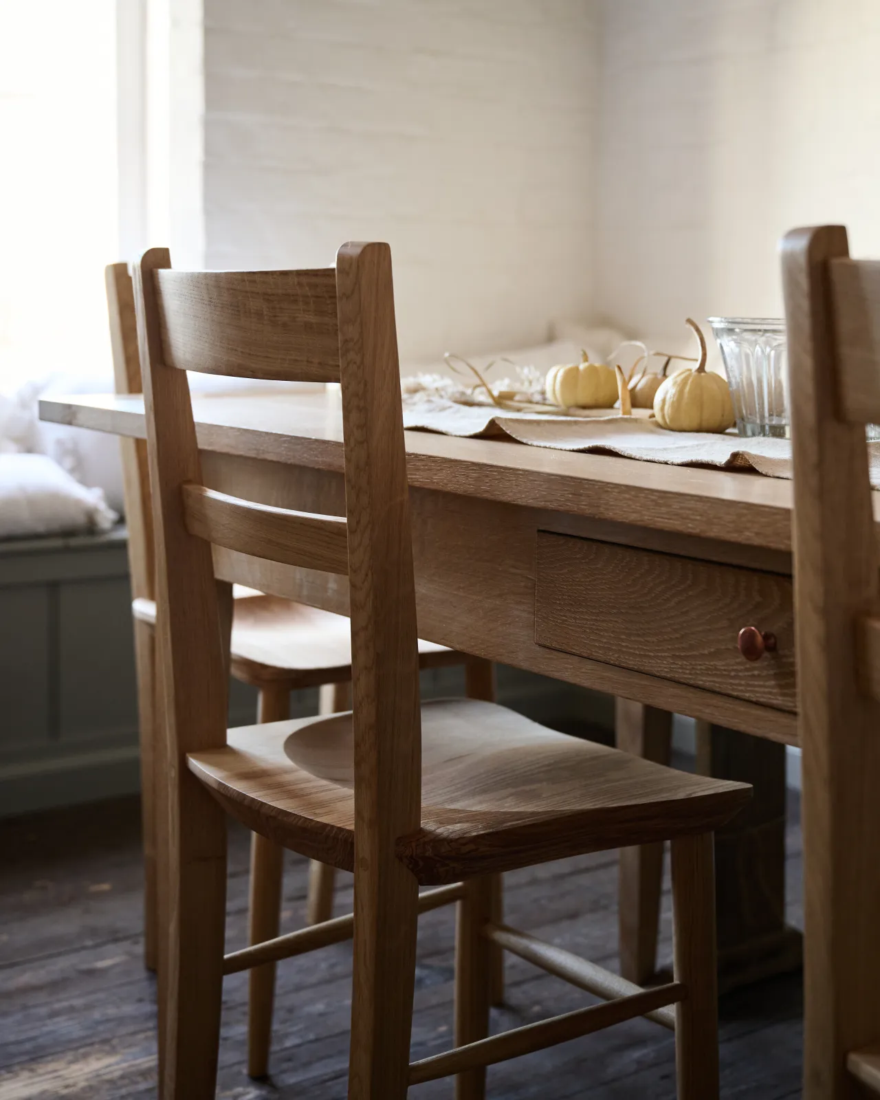 An oblique view of the back of a mid-century-style dining chair with a sculpted ash seat pan and a bar-back oak backrest.