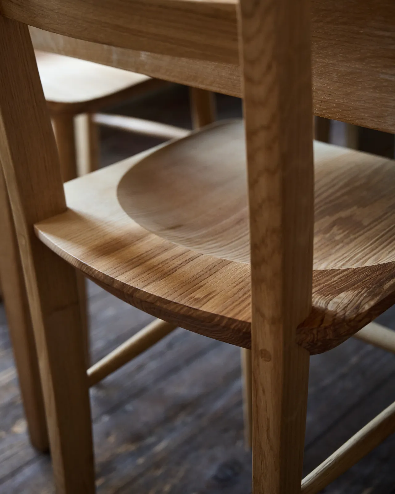 A close-up oblique view of the back of a sculpted ash seat pan from a mid-century-style dining chair.