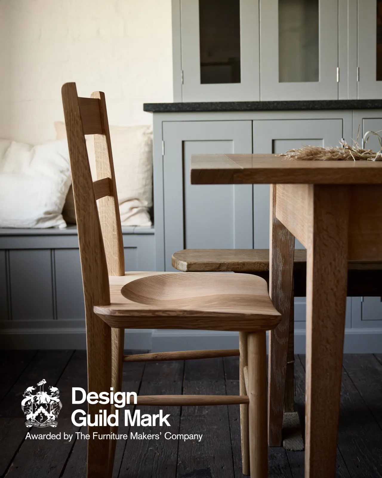 A profile view of a mid-century-style dining chair with a sculpted ash seat pan and oak legs and frame. A logo in the bottom corner reads 'Design Guild Mark; Awarded by the Furniture Makers' Company'.