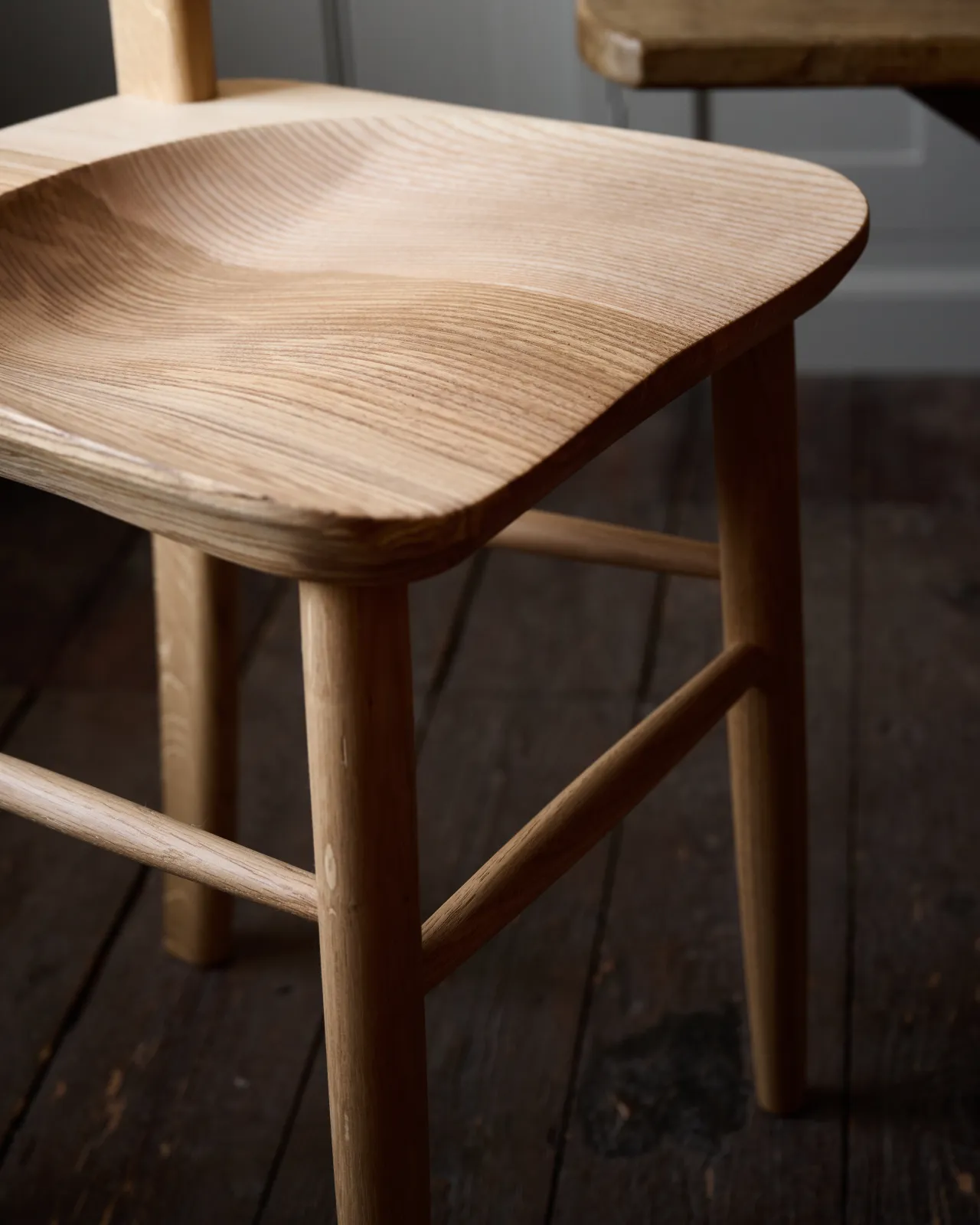 A close-up oblique view of a sculpted ash seat pan from a mid-century-style dining chair.