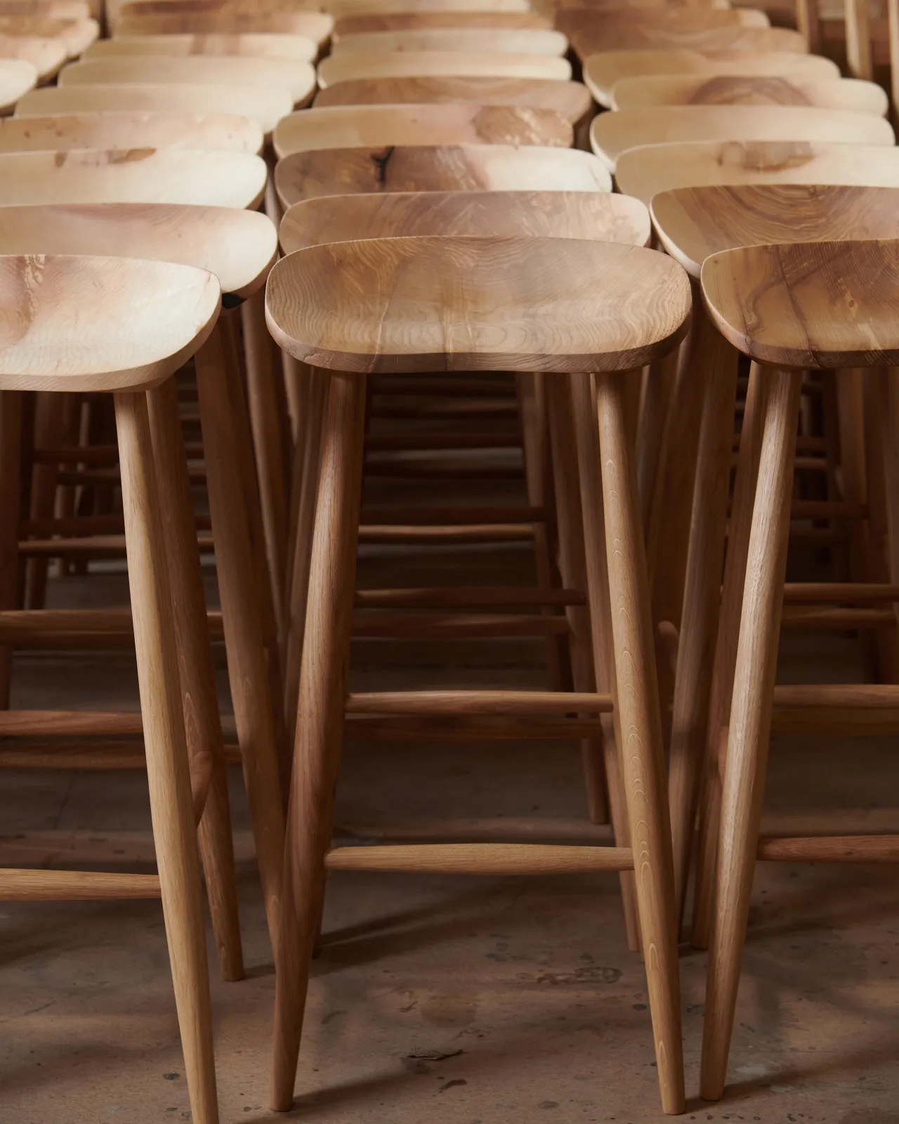 A straight-on view of a large set of mid-century-style bar stools with a sculpted ash seat pans and oak legs. The wood grain of each seat pan is slightly different in tone and pattern.