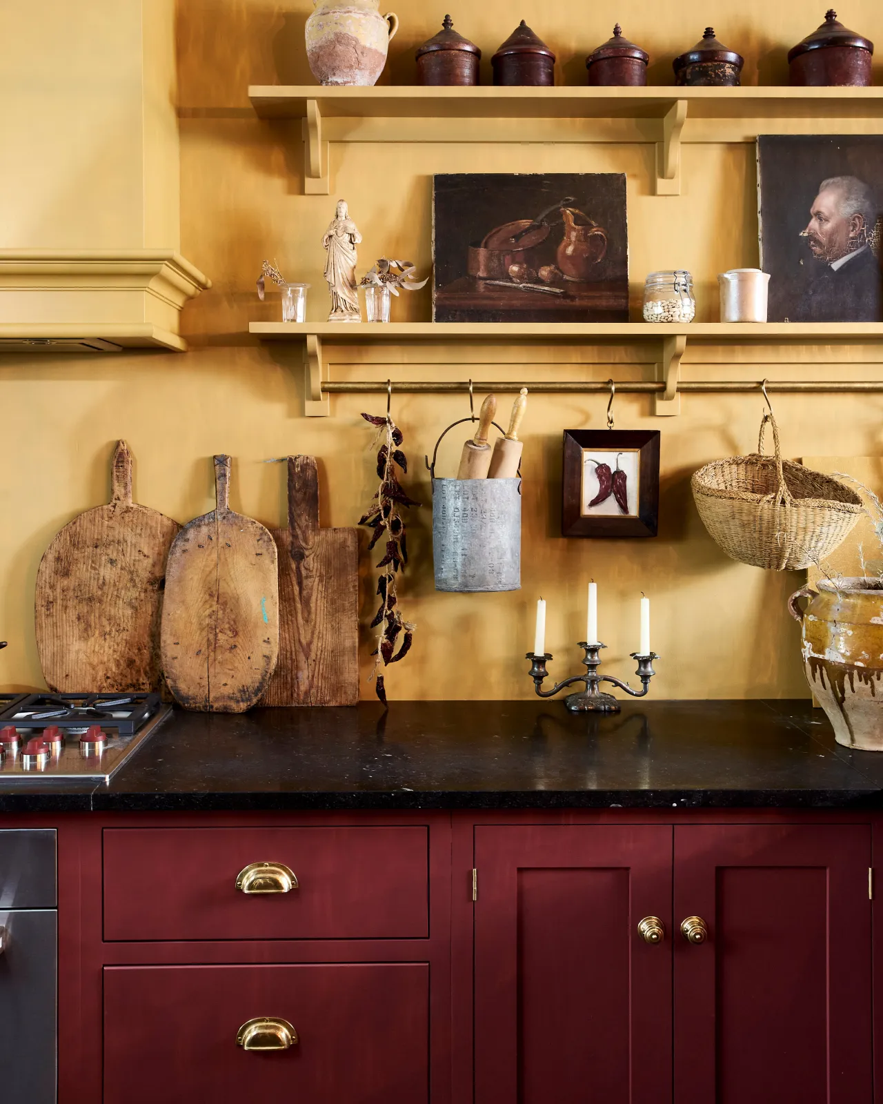 A straight-on view of an eclectic Shaker-style kitchen with yellow walls, red painted cabinetry, black granite worktops and Victorian-inspired ornate doorknobs in a warm burnished brass finish.
