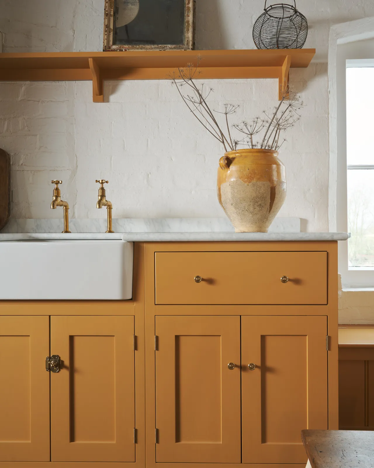 A straight-on view of a yellow painted Shaker-style kitchen sink cupboard with small Victorian-inspired doorknobs in a warm burnished brass finish.