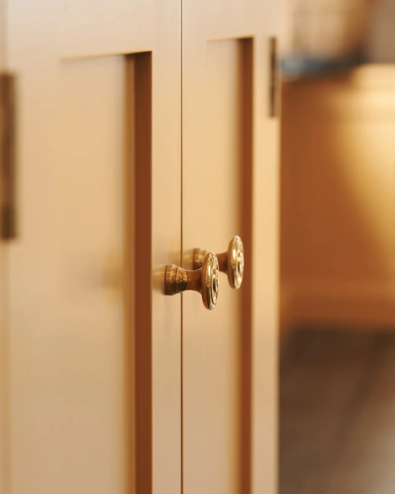 A close-up profile view of a pair of small Victorian-inspired doorknobs in a warm burnished brass finish, fitted to a yellow painted cupboard doors.
