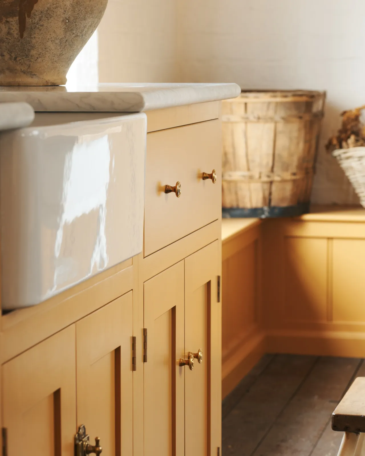 An oblique view of a yellow painted Shaker-style kitchen sink cupboard with small Victorian-inspired doorknobs in a warm burnished brass finish.