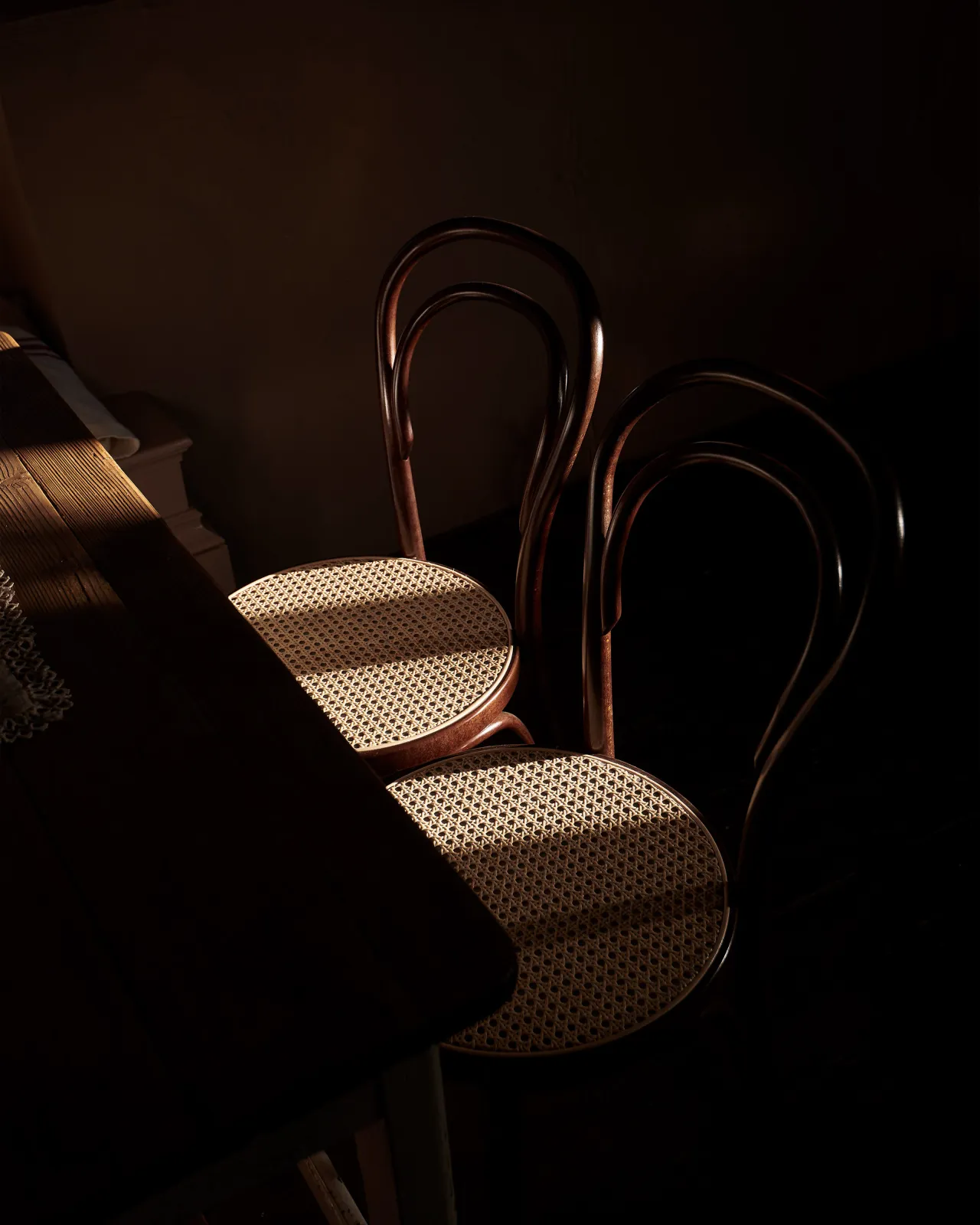 A dark room with two café-style bentwood chairs with dark stained frames and light woven rattan seat mesh.