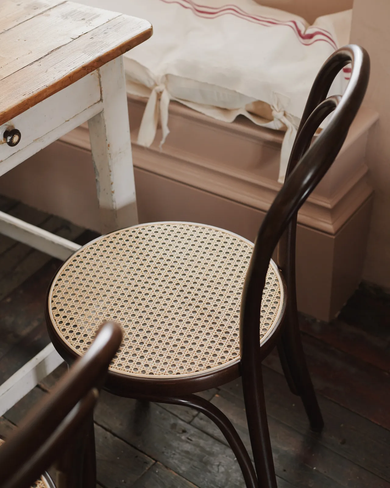 An oblique view of a café-style bentwood chair with a dark stained frame and light woven rattan seat mesh.