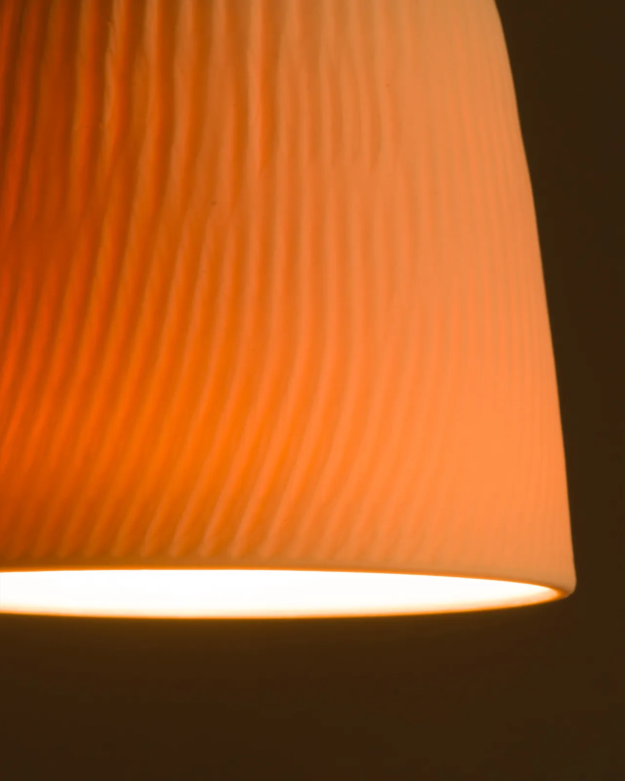 A close-up view of an unglazed chattered beaker porcelain pendant with the light on, showing the warm red glow of the translucent surface.