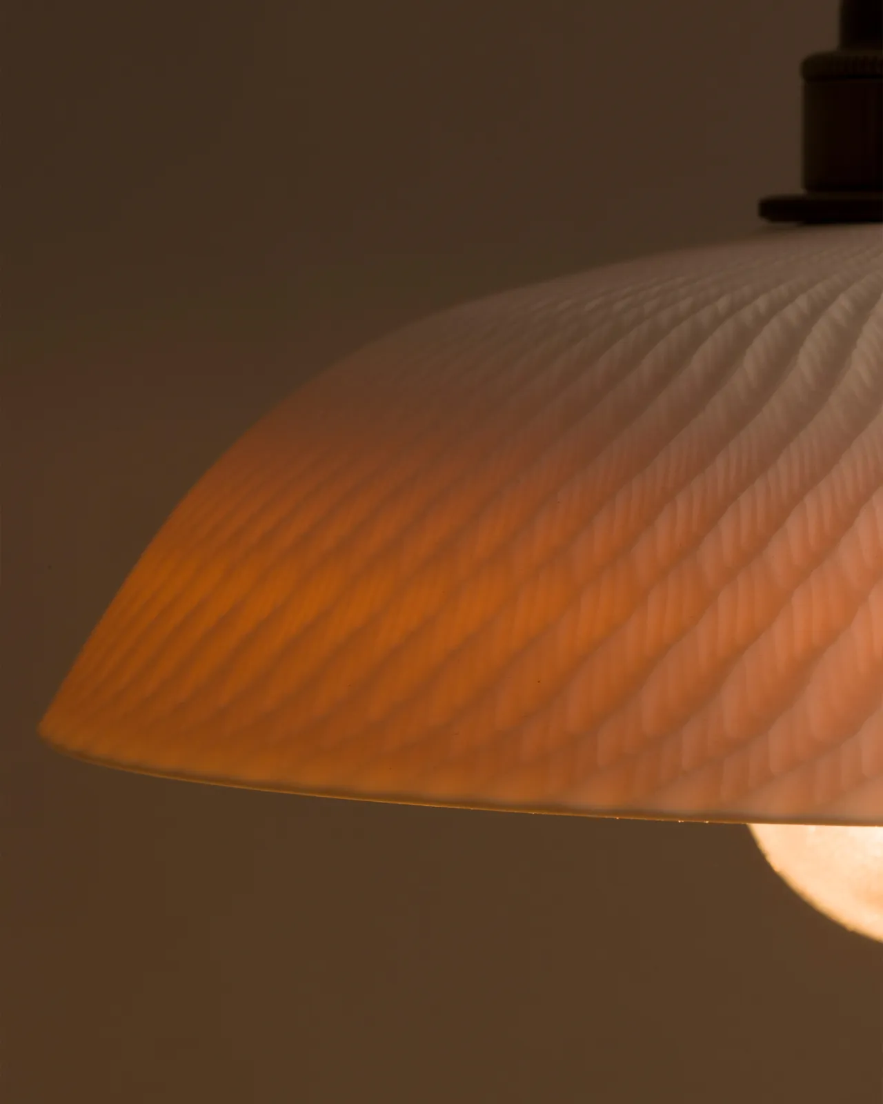 A close-up view of an unglazed chattered skullcap porcelain pendant with the light on, showing the warm red glow of the translucent surface.