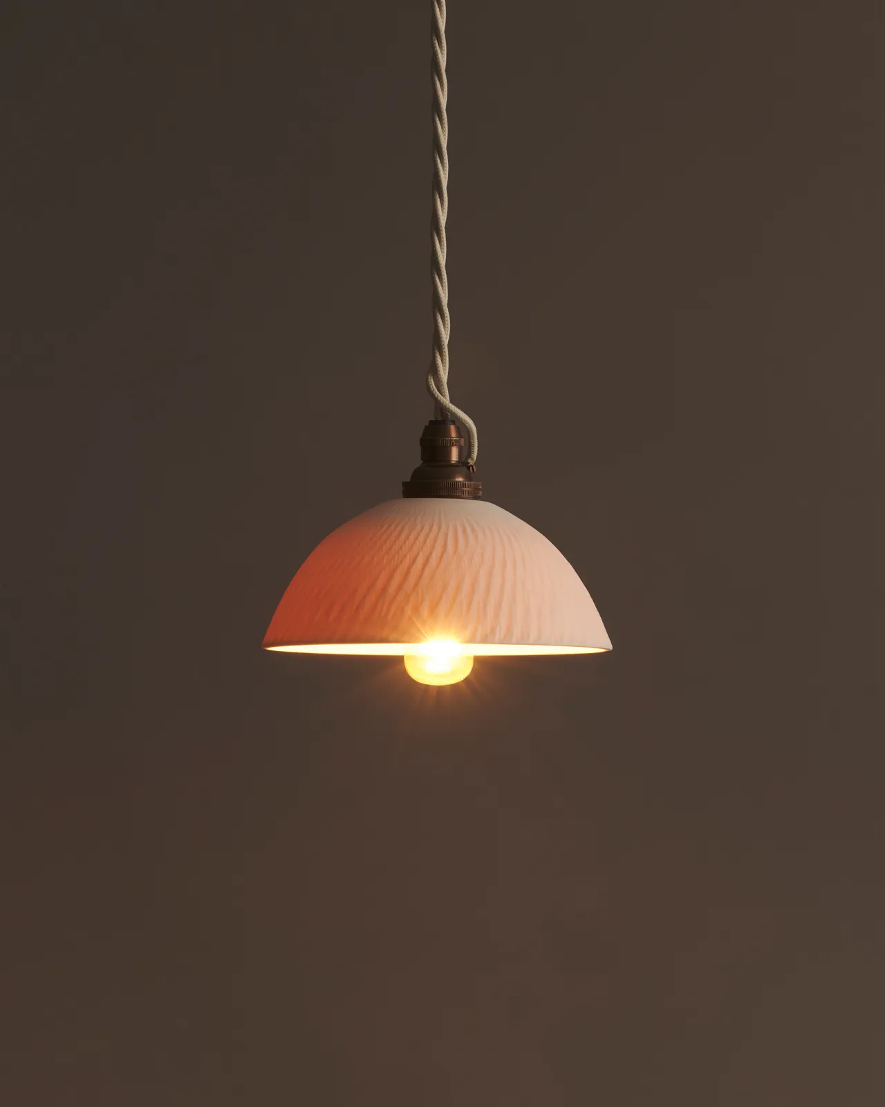 A chattered rice bowl porcelain pendant with the light on, showing the warm red glow of the translucent surface.